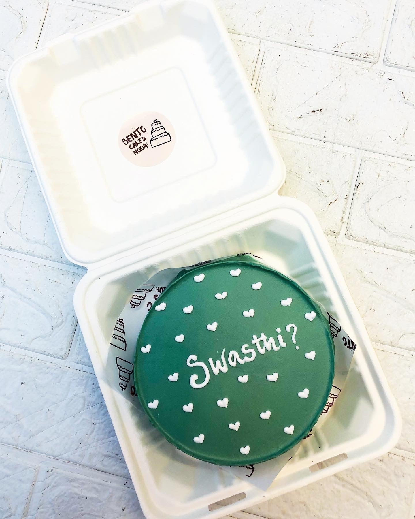 A dark green bento cake with little white hearts design on its too and a text "Swati?" written with white icing.
