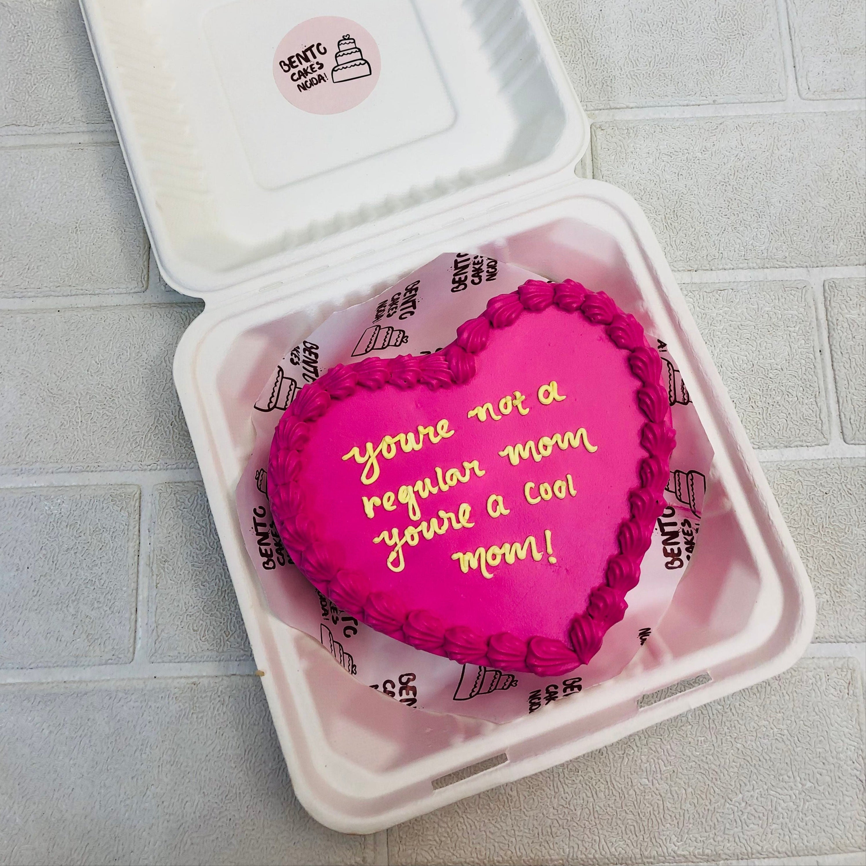 Dark Pink Heart shape cake in a  bento box with pink boundary design and a text with yellow color written on it.