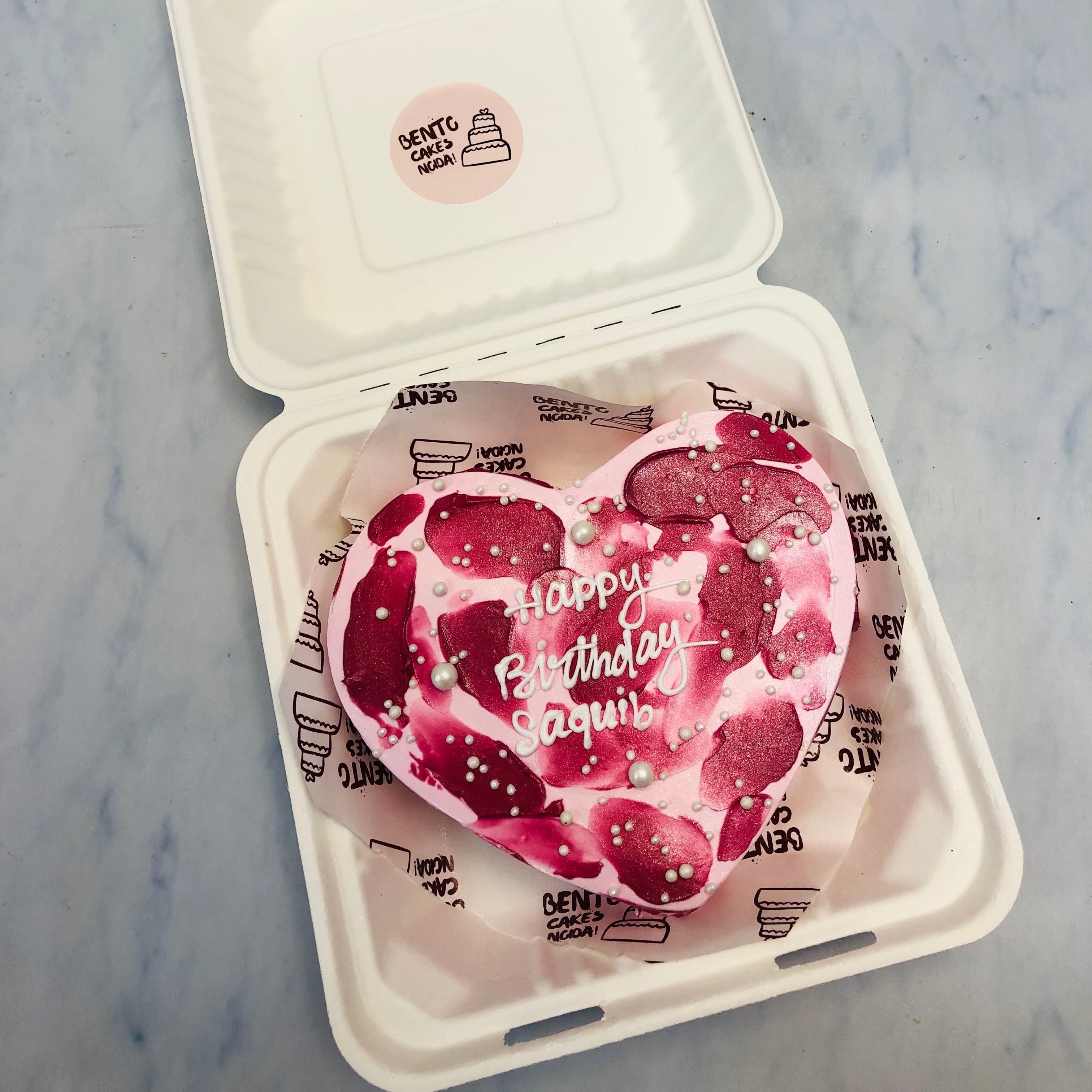 A light pink heart shape cake with dark pink shades o it and a text with white color written on it.