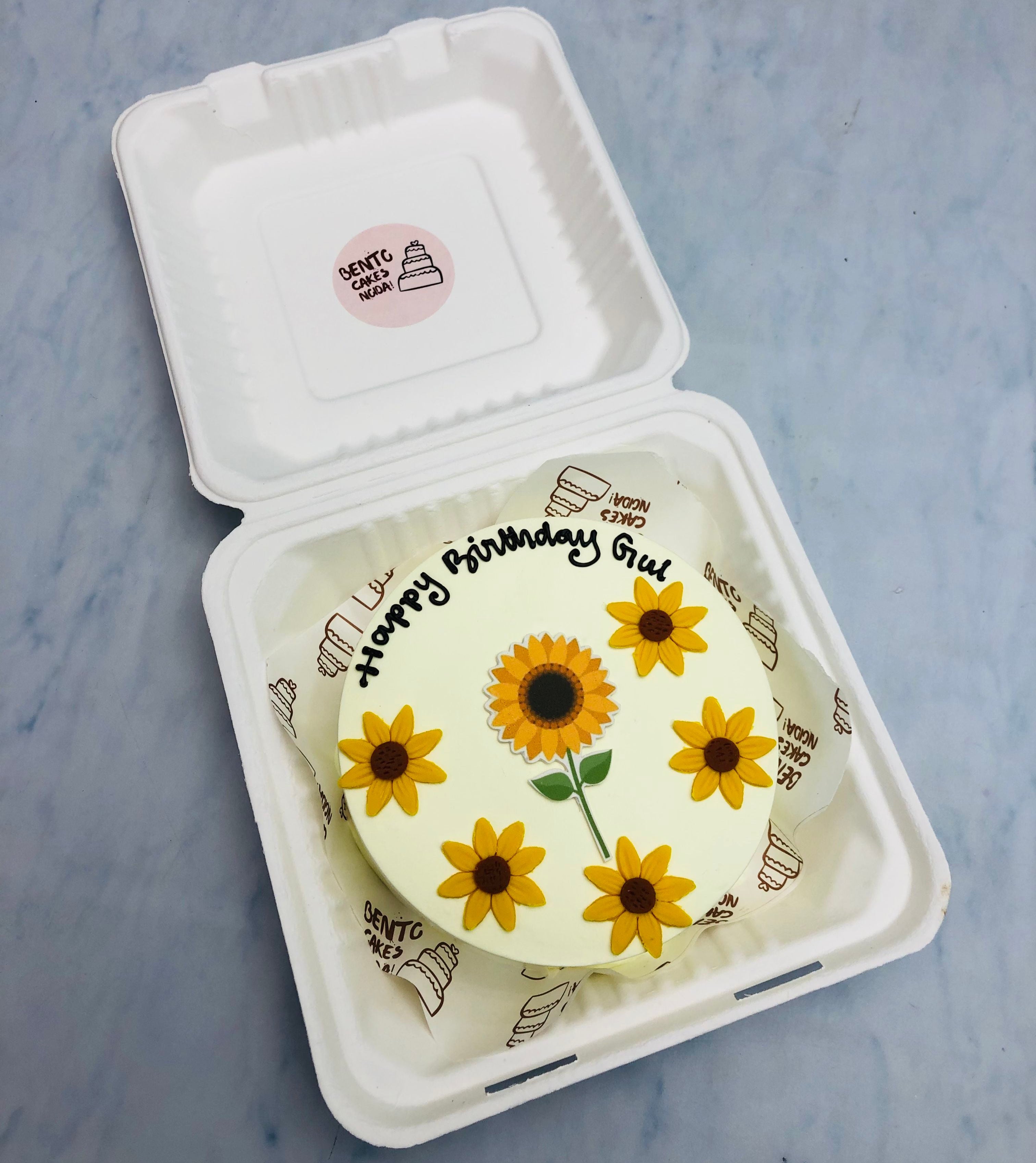 A white bento cake having sunflowers design with fondant and a flower print in the center.