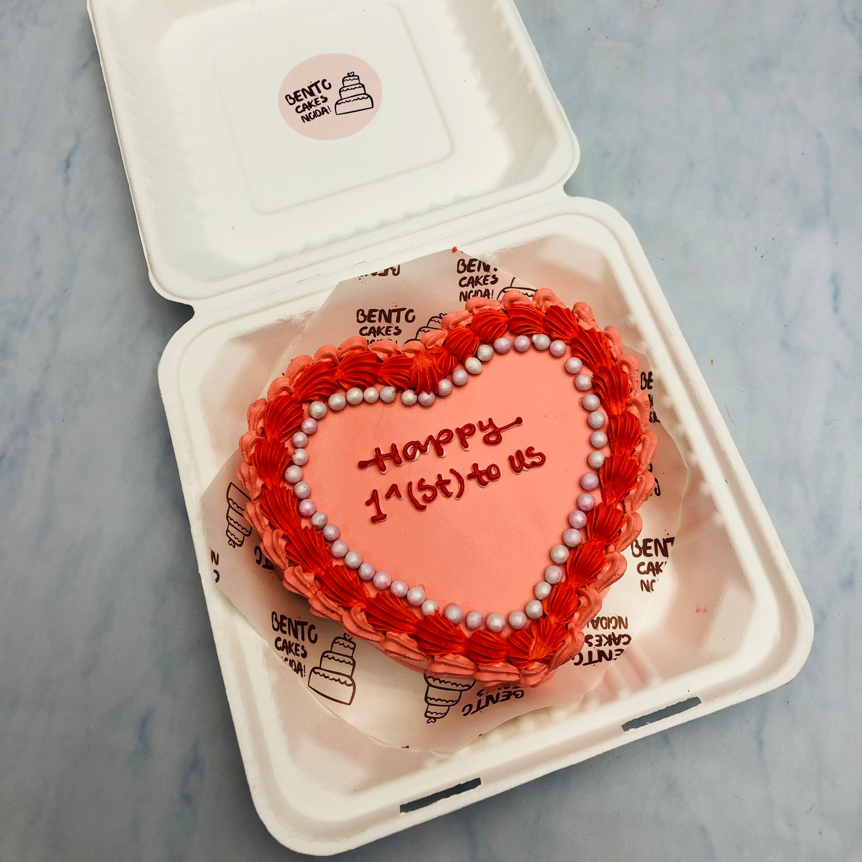 A light red heart shape designer cake is beautifully decorated with red iving and a loving text written on it.