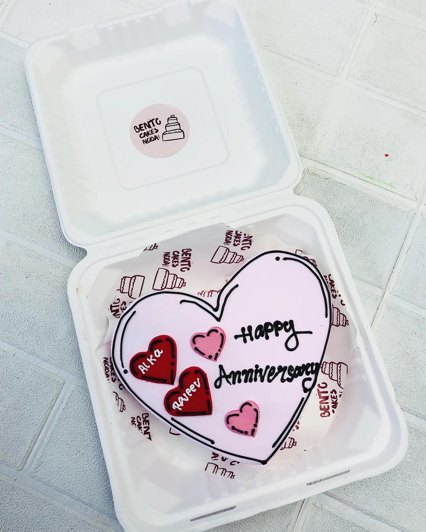 A white heart shape cake designed with black icing and red - pink color hearts on the cake. 