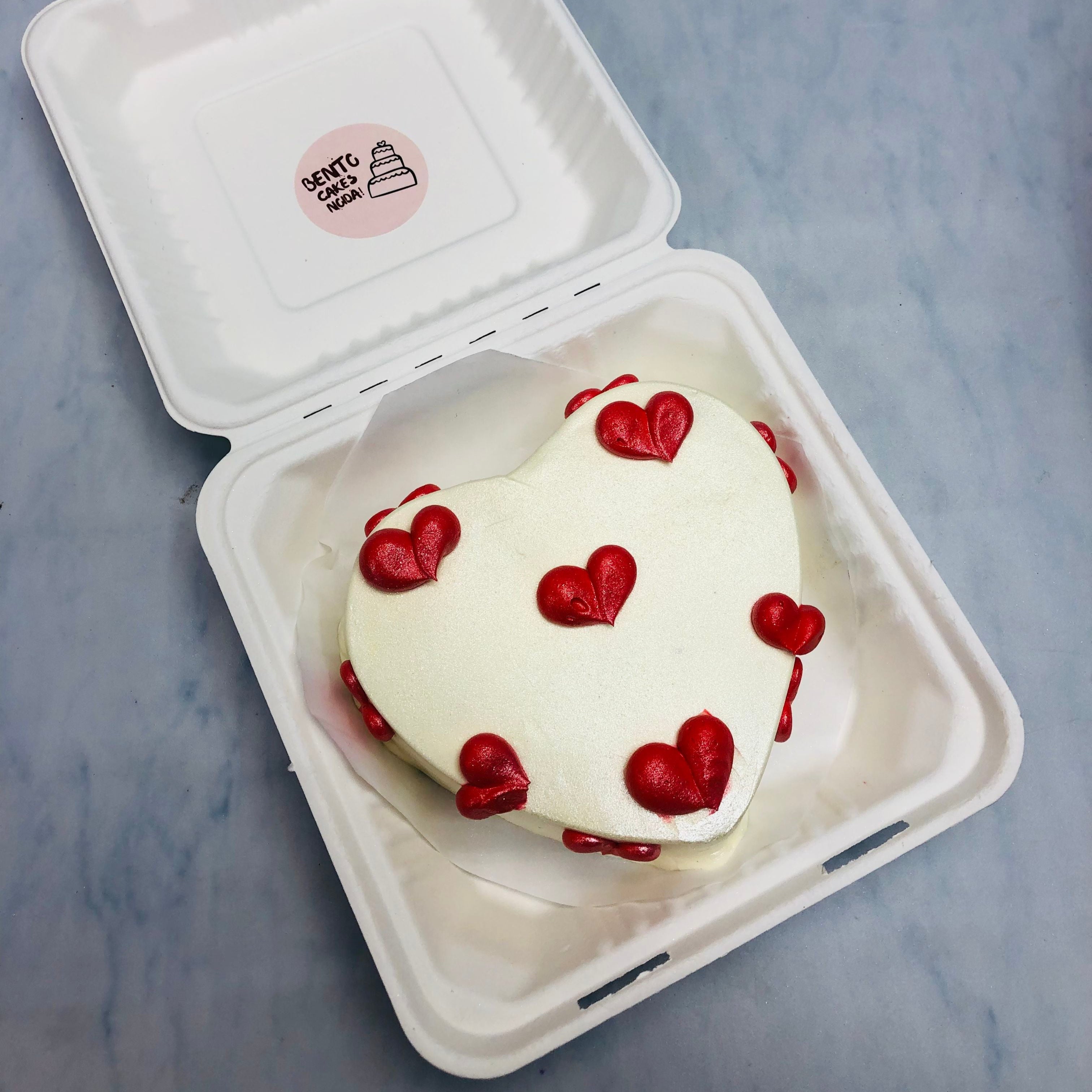 A shiny white heart shape cake with delightful red hearts design all over the cake.