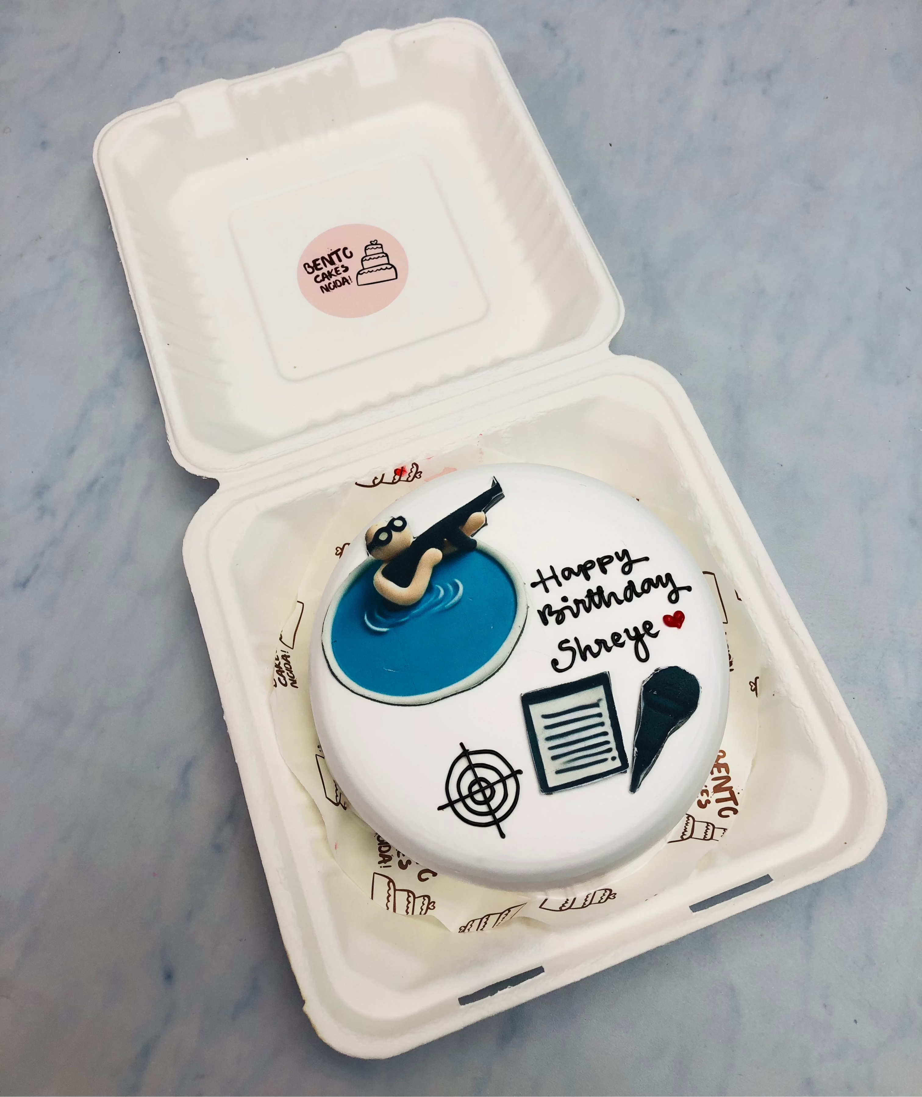 A white bento cake having a detective theme with his gun and target.