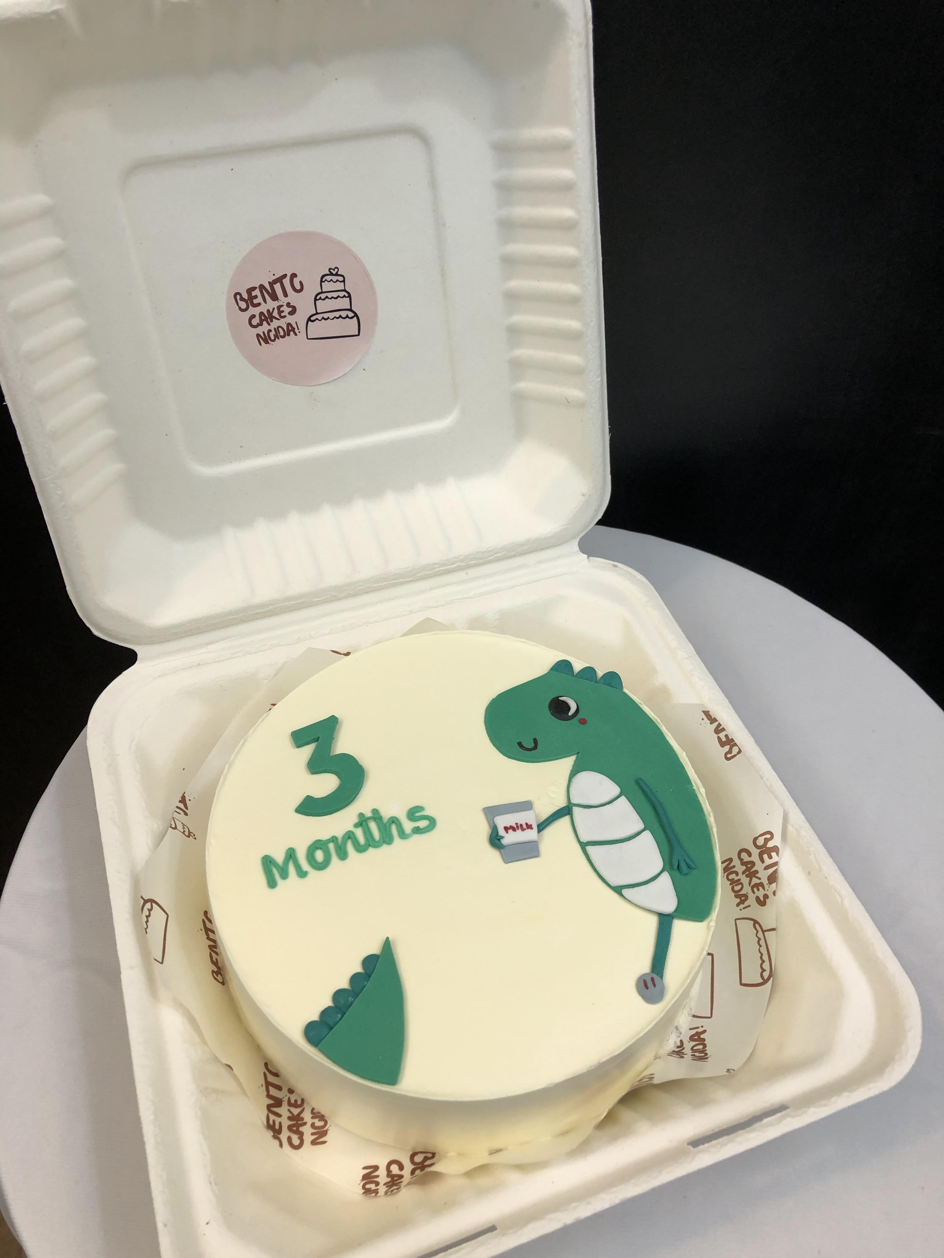A offwhite cake with dianosaur design with 3 months text.