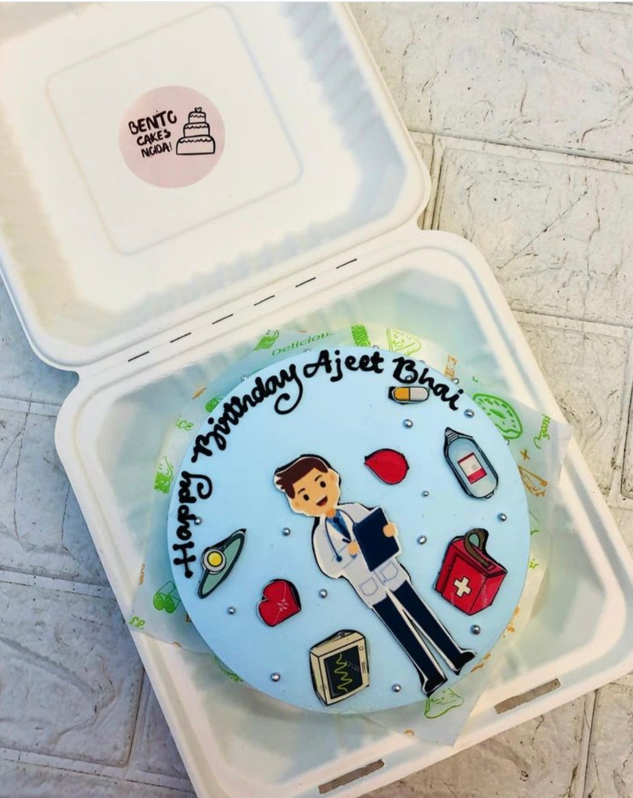 A light blue bento cake is designed for doctor's birthday having doctors kit and a doctor sticker.