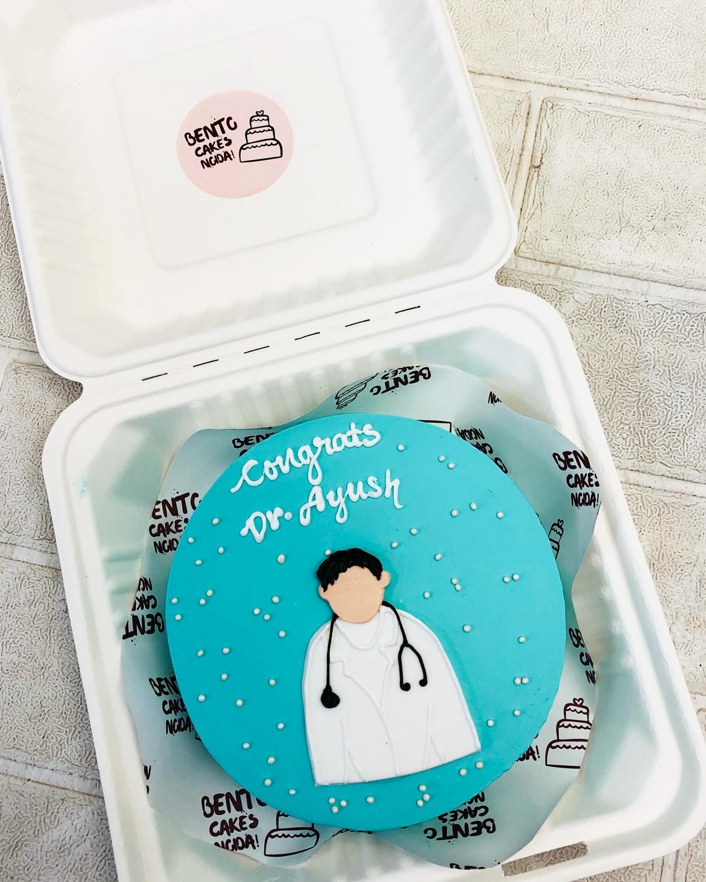 A skyblue bento cake is designed for a doctor's birthday having fondant design of men.