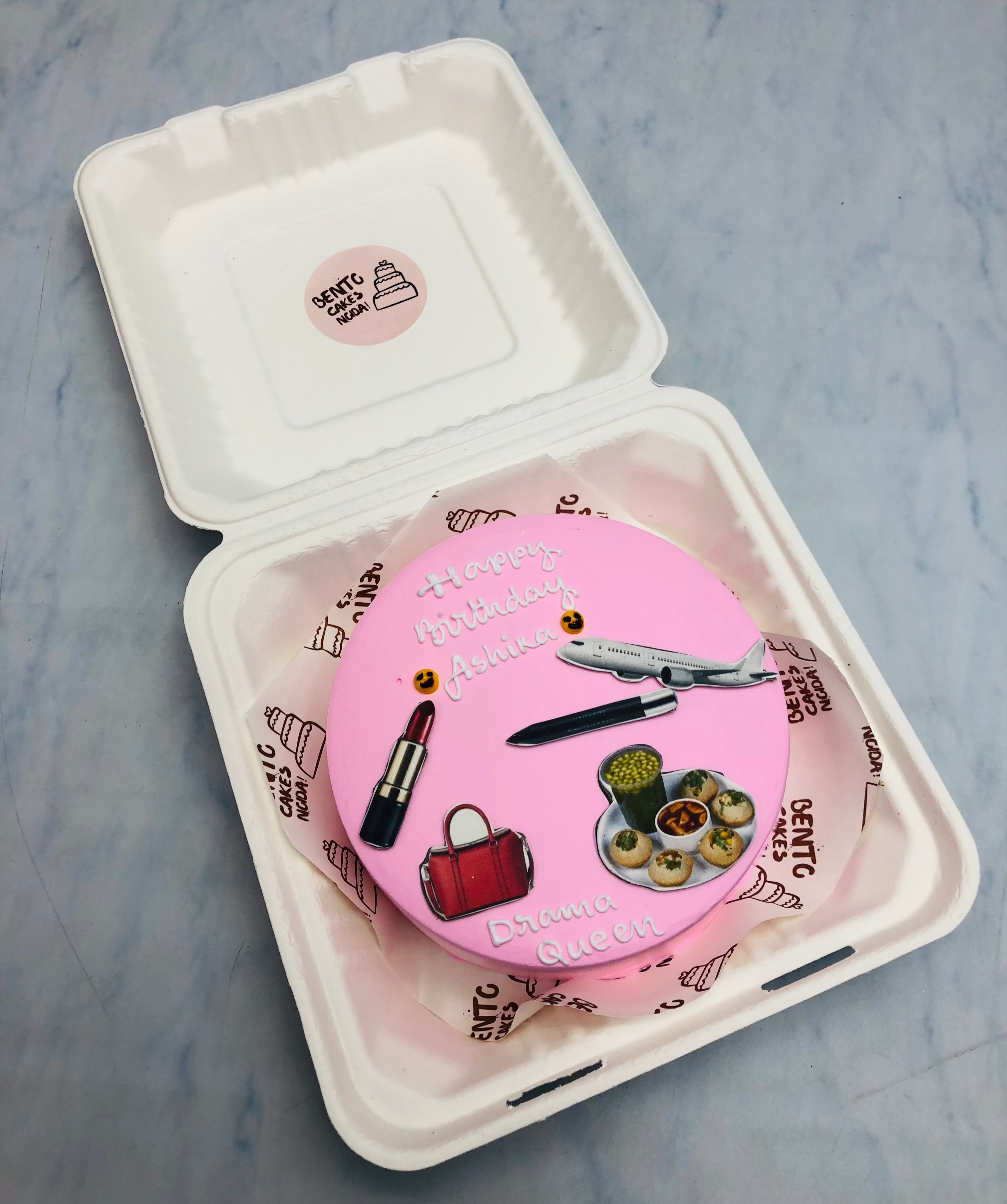 A light pink bento cake with a drama queens birthday and having a makeup, foody and travelling theme.