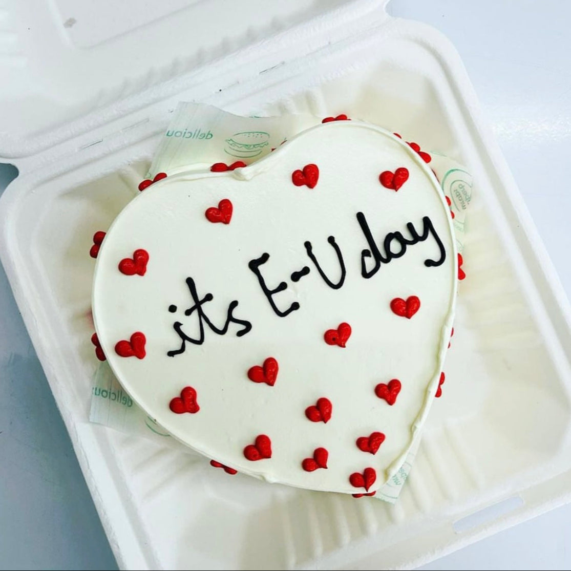 A heart-shaped cake adorned with the words "It's EU Day" elegantly written on its surface.