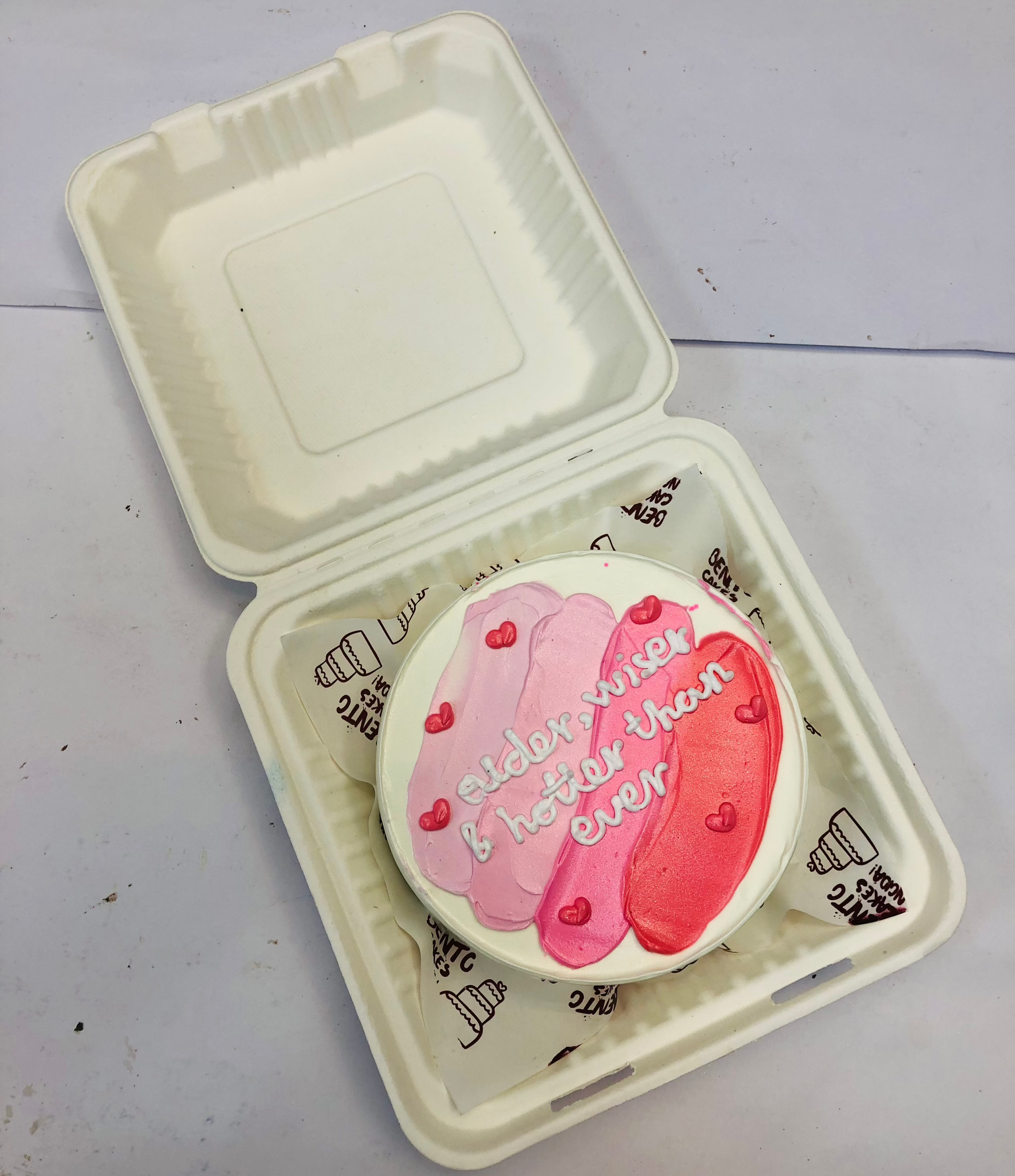 A white bento cake with 3 colors of pink shades with a white text written on it.