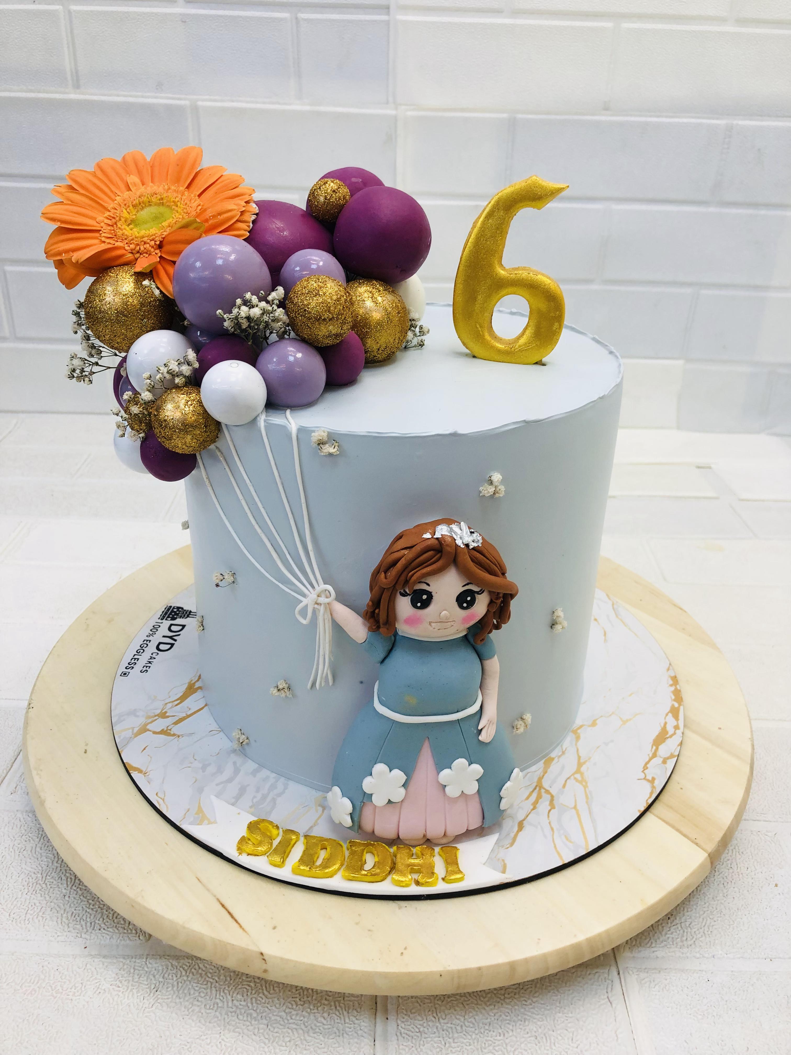A beautifully decorated birthday cake for a 6-year-old named Siddhi. The cake features light blue fondant with a fondant figure of a girl in a blue dress holding white balloon strings. The top is adorned with a cluster of purple, gold, and white balloons, along with an orange flower. A golden number 6 topper is placed on the cake, and the name 'Siddhi' is written in gold letters at the base.