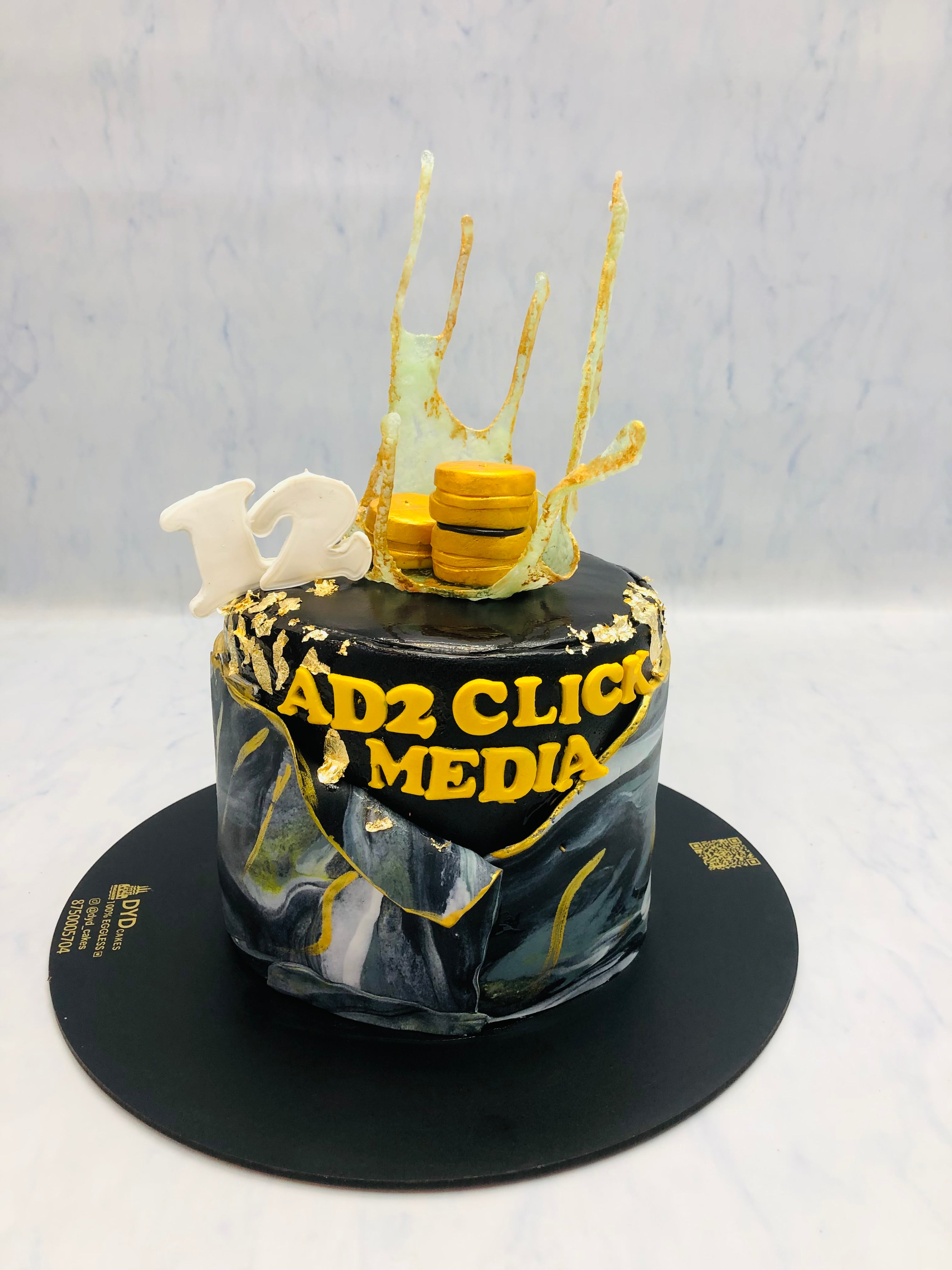 A black and gold cake with the text "AD2 Click Media" and the number "12" on top, decorated with gold coins and sugar art.