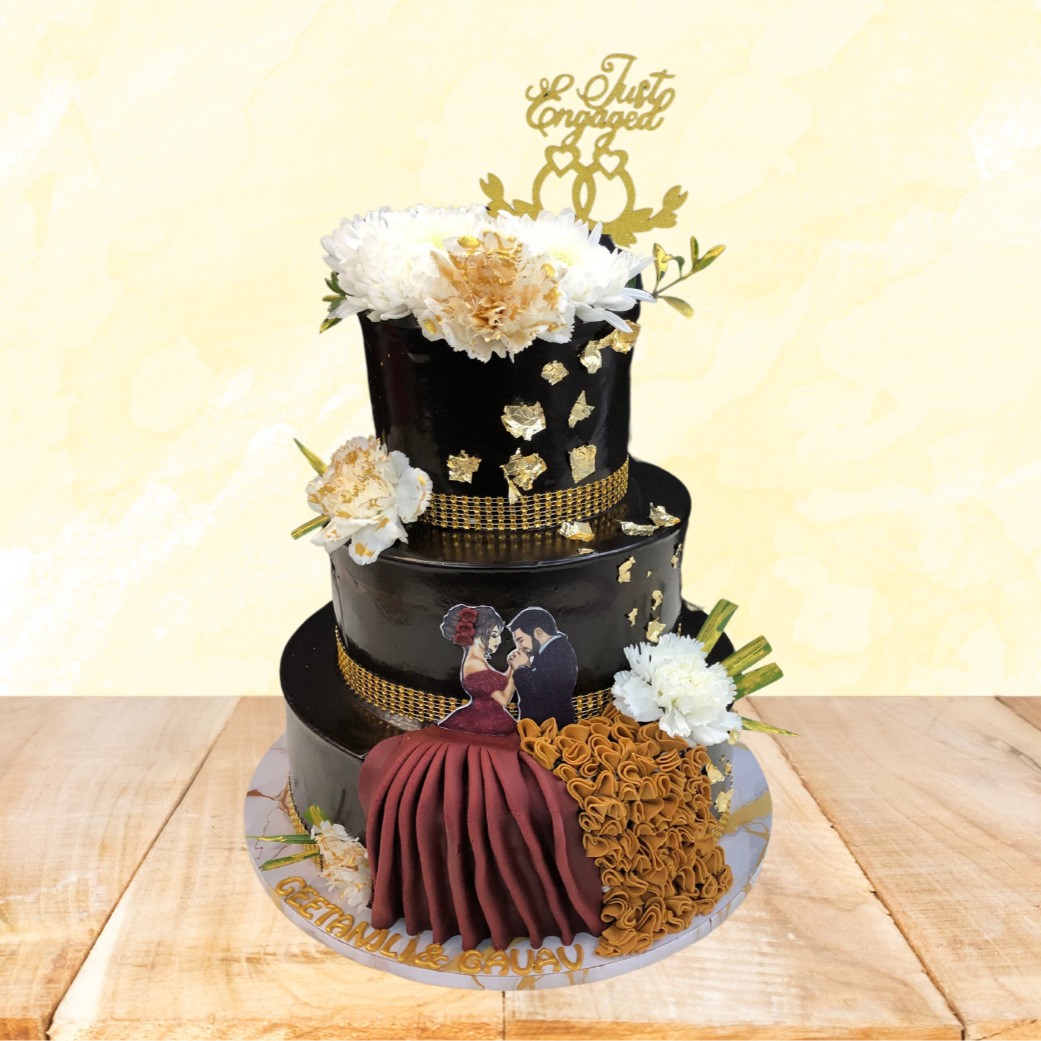 A three-tiered black engagement cake adorned with gold accents, white flowers, and a "Just Engaged" topper. The bottom tier features a fondant couple in an embrace, with the names "Geetanjali & Gavrav" written on the cake board.