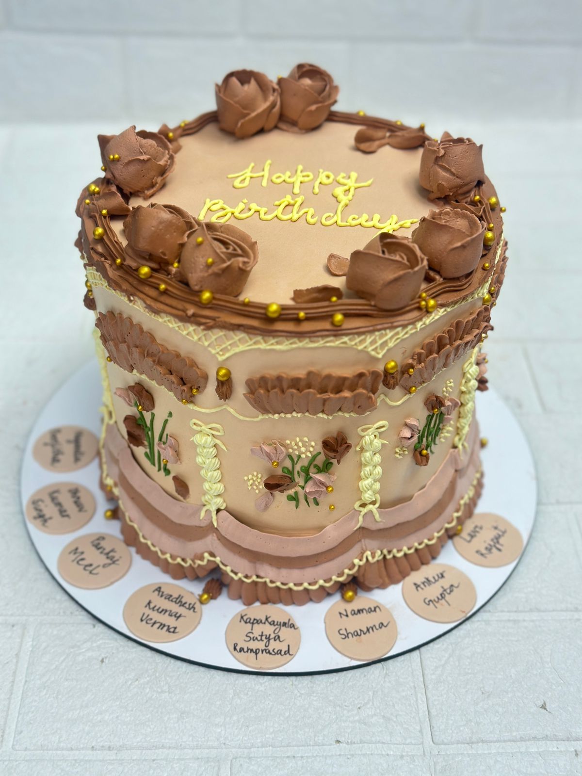 A beautifully decorated birthday cake with floral designs and personalized names on the base.