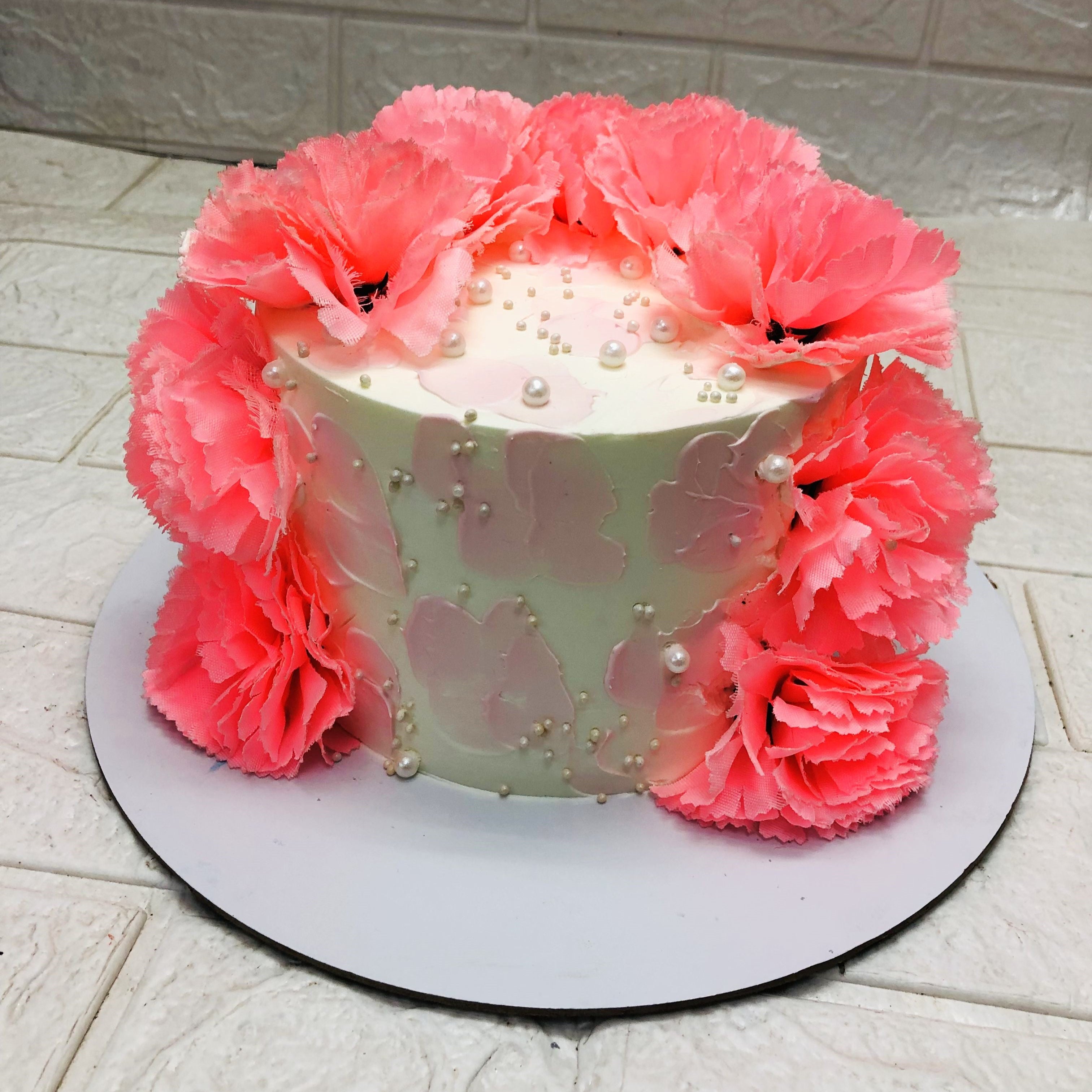 A beautifully decorated cake adorned with vibrant pink flowers and pearl-like decorations on a white base.