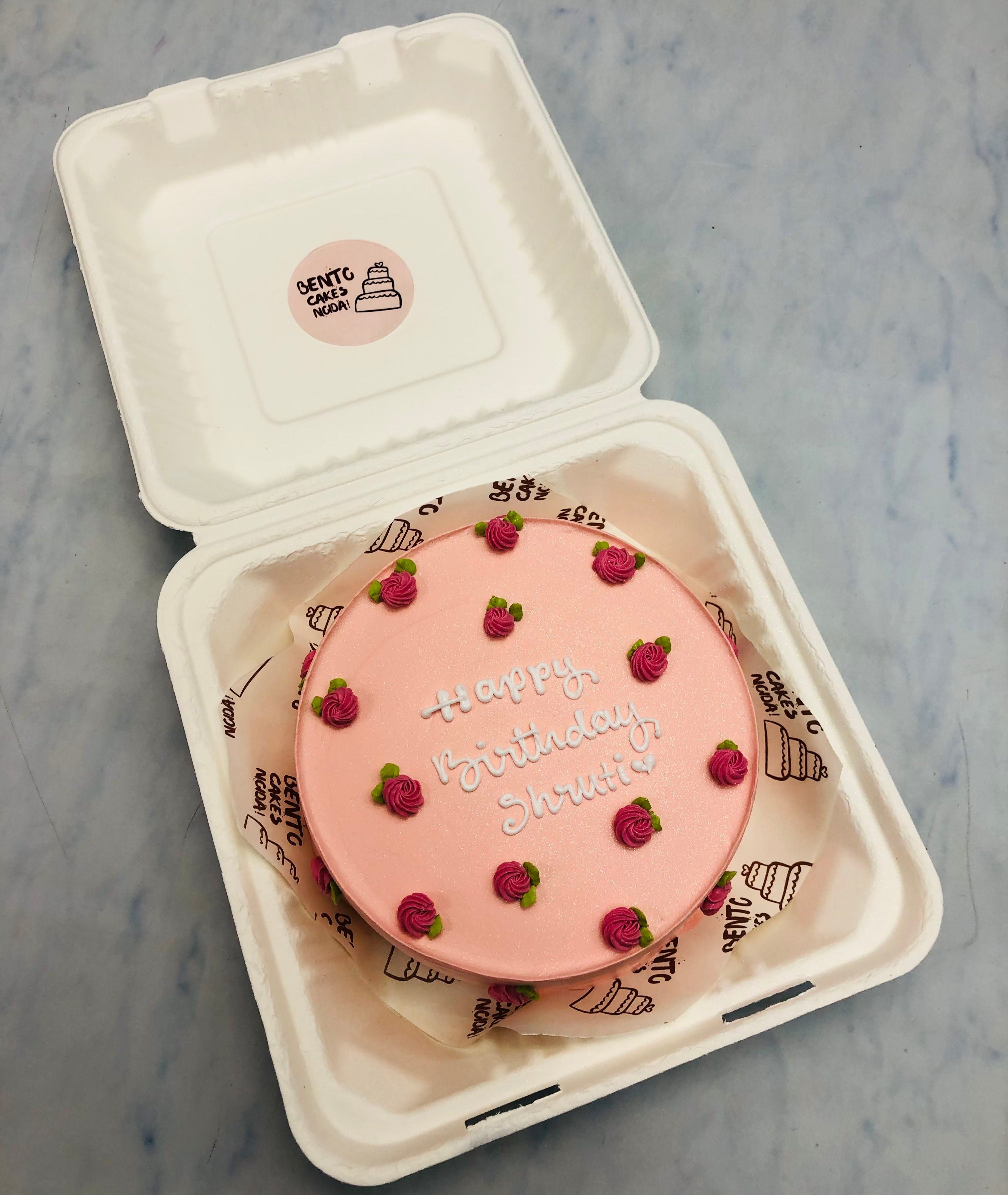 A beautifully crafted pink birthday cake with "Happy Birthday Shruti" written in white icing, adorned with delicate pink rose designs.