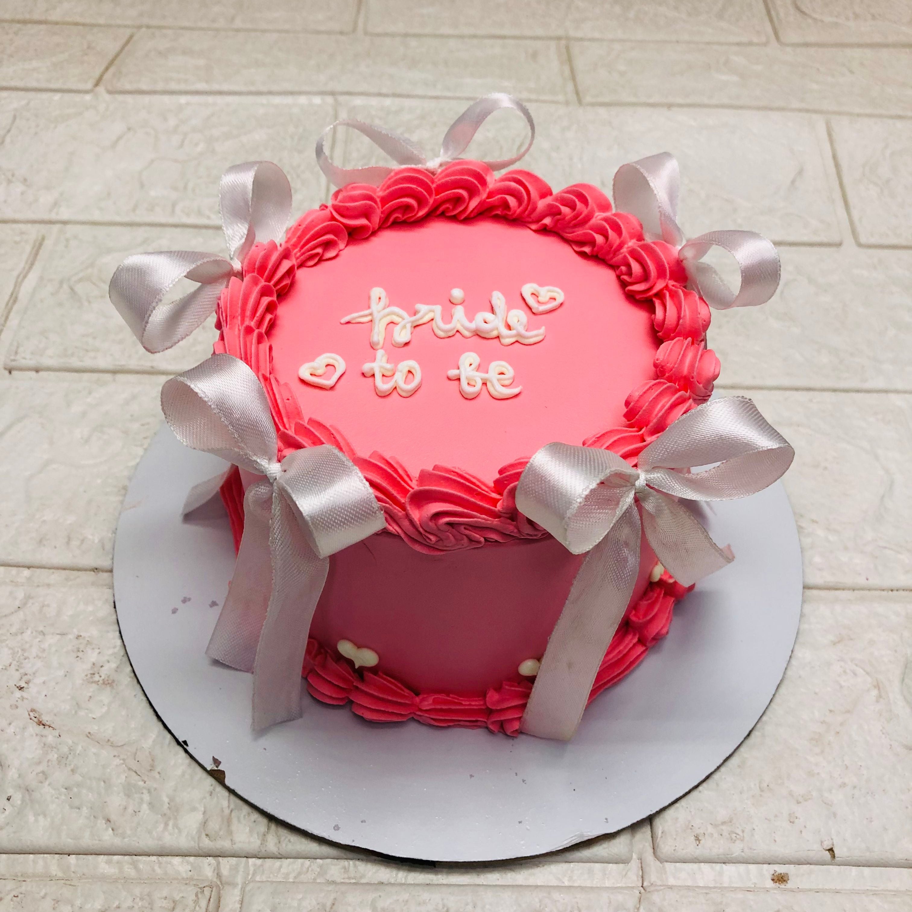A pink bridal shower cake with white bows and the words 'bride to be' written on top.