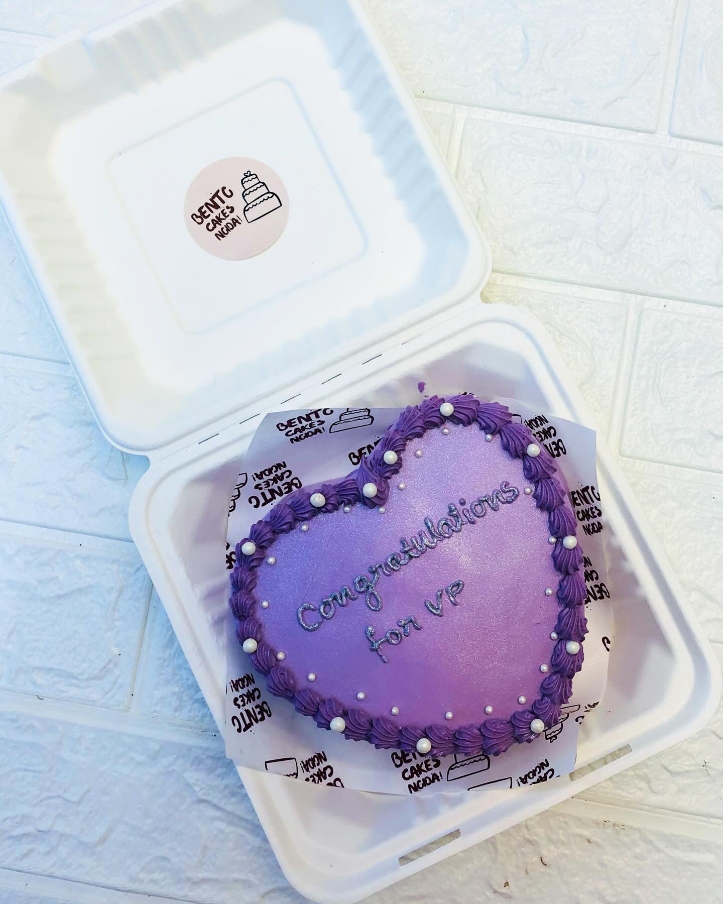 A dark purple heart shape cake with purple text on it.