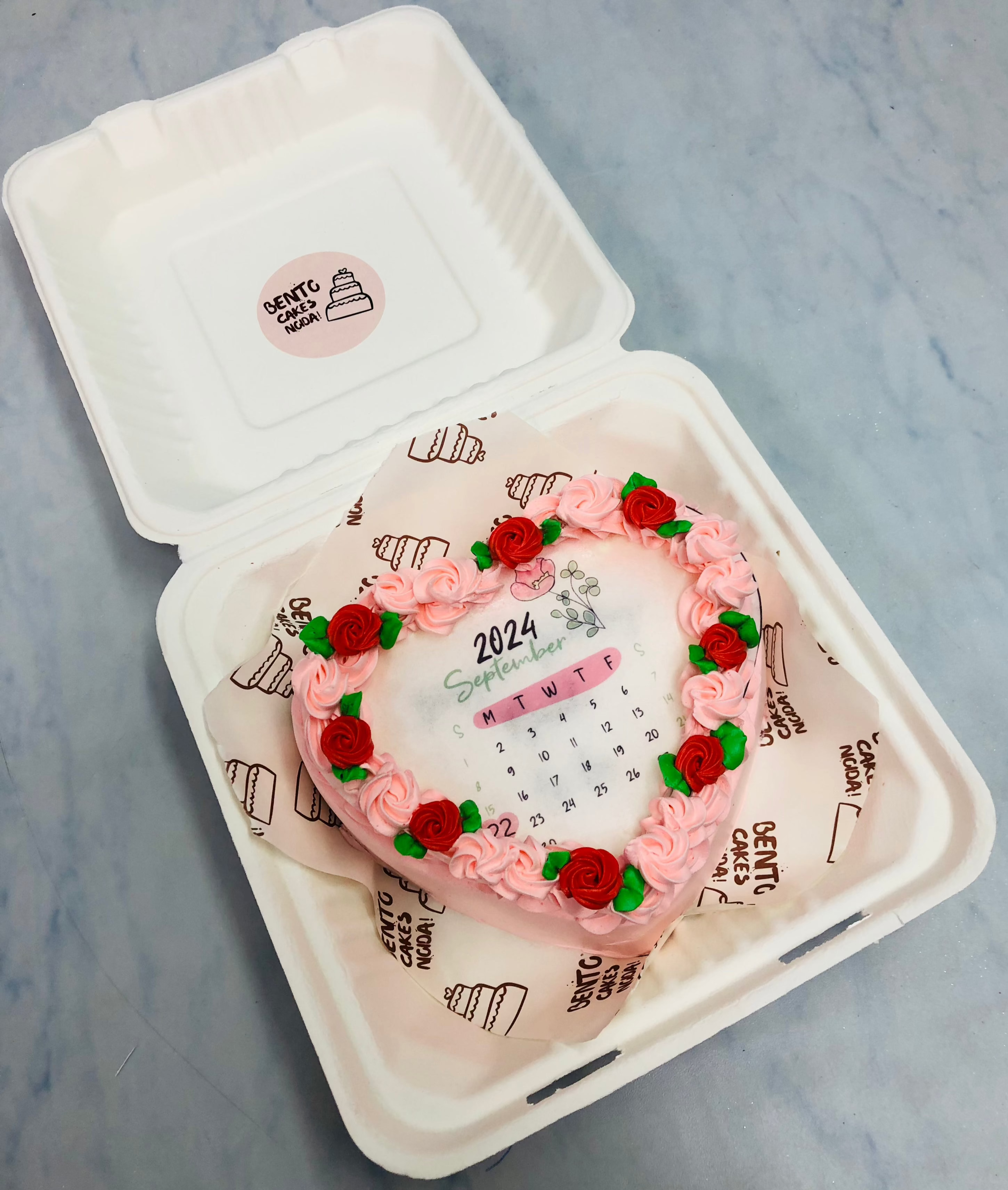 A pink-red floral heart shape fire bento cake having calendar design. 