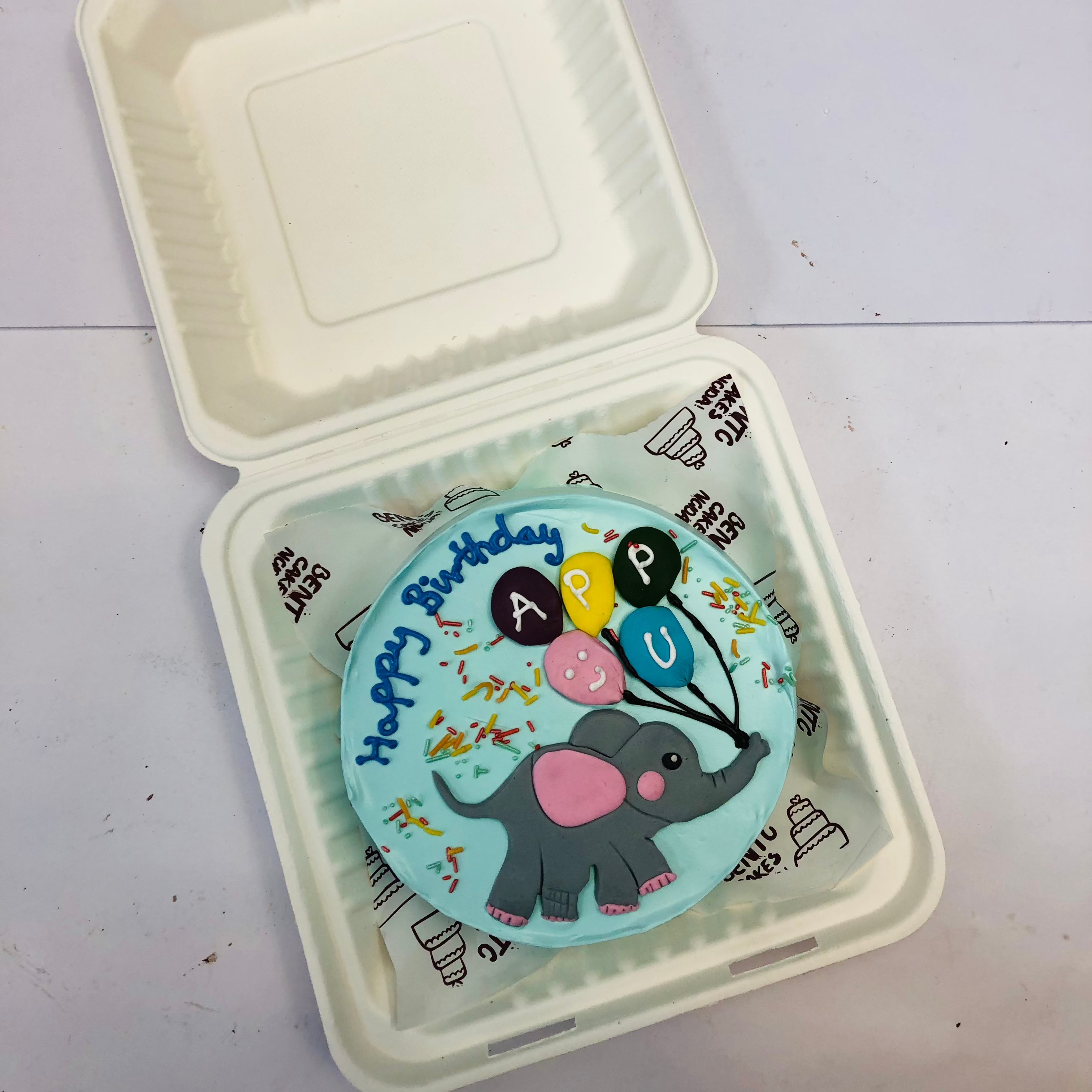 A cool blue bento cake with fondant elephant design having colorful baloons for baby birthday.