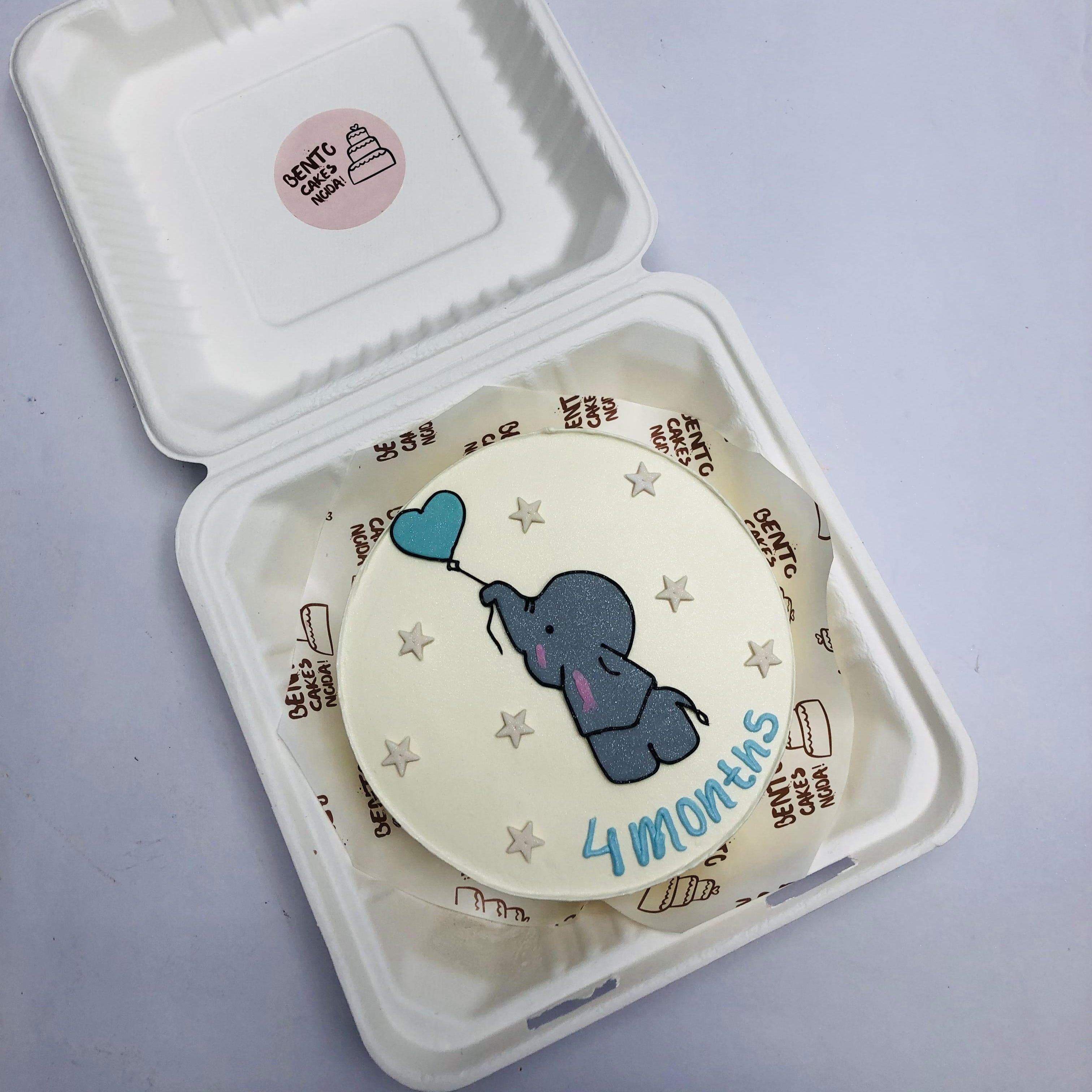 A cute baby elephant having blue heart balloon on a whit bento cake.