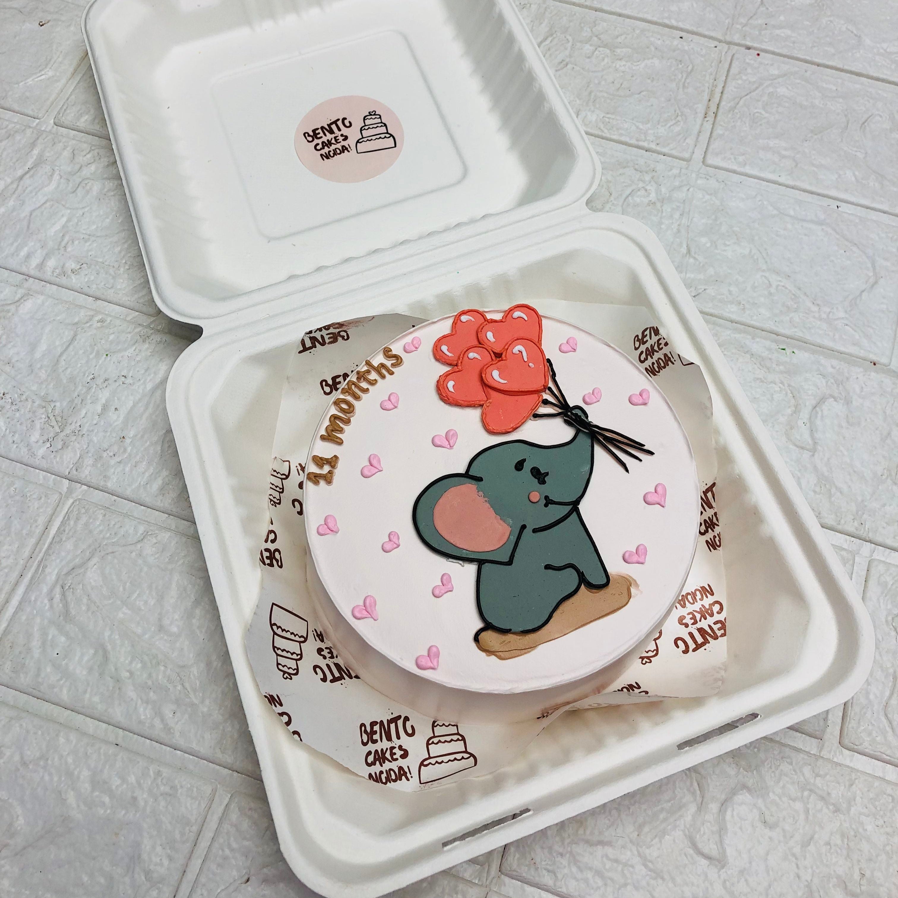 A white color cake with a baby elephant drawing andtaken balloon.