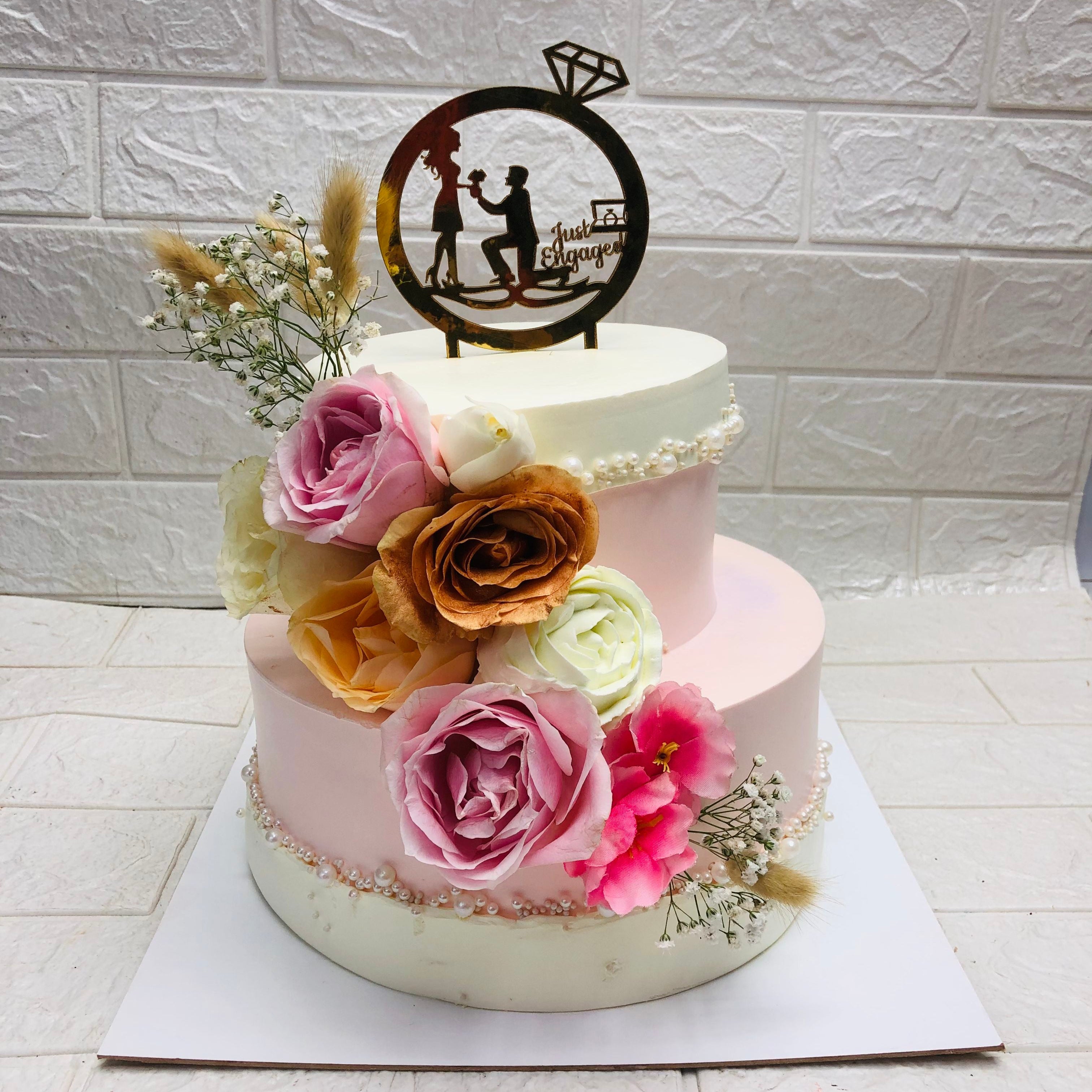 A 2 tier beautifully designed engagement cake decorated with colorful flowers on side.