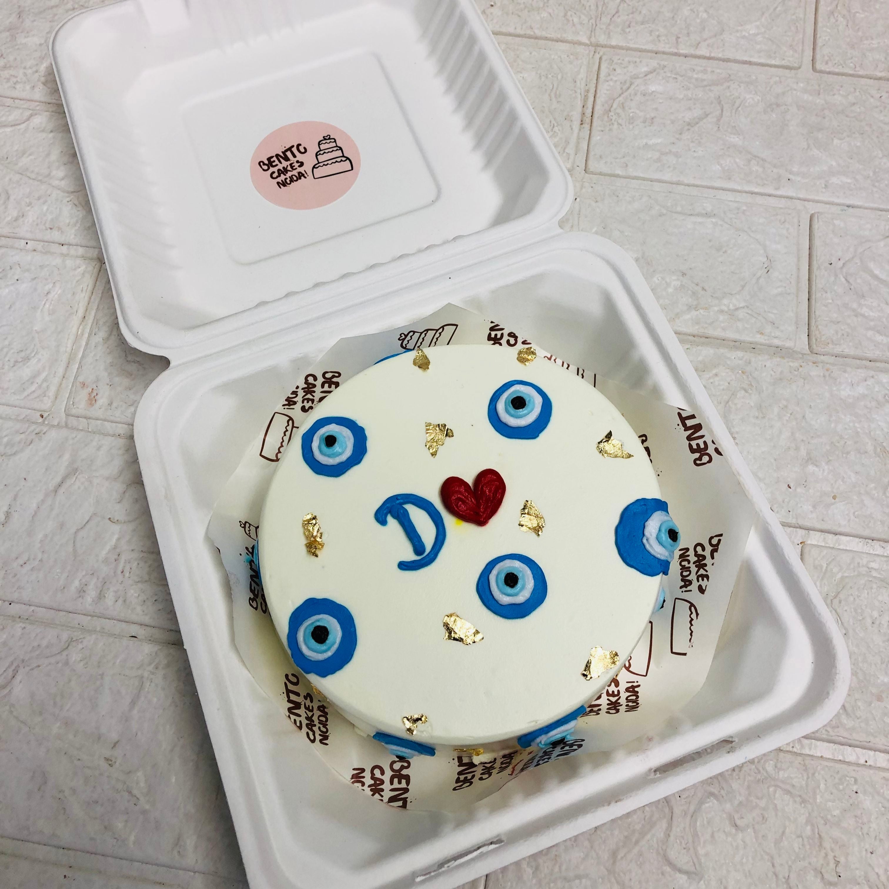 A cake with menacing eyes, presented in an elegant box, creating a whimsical yet eerie atmosphere.