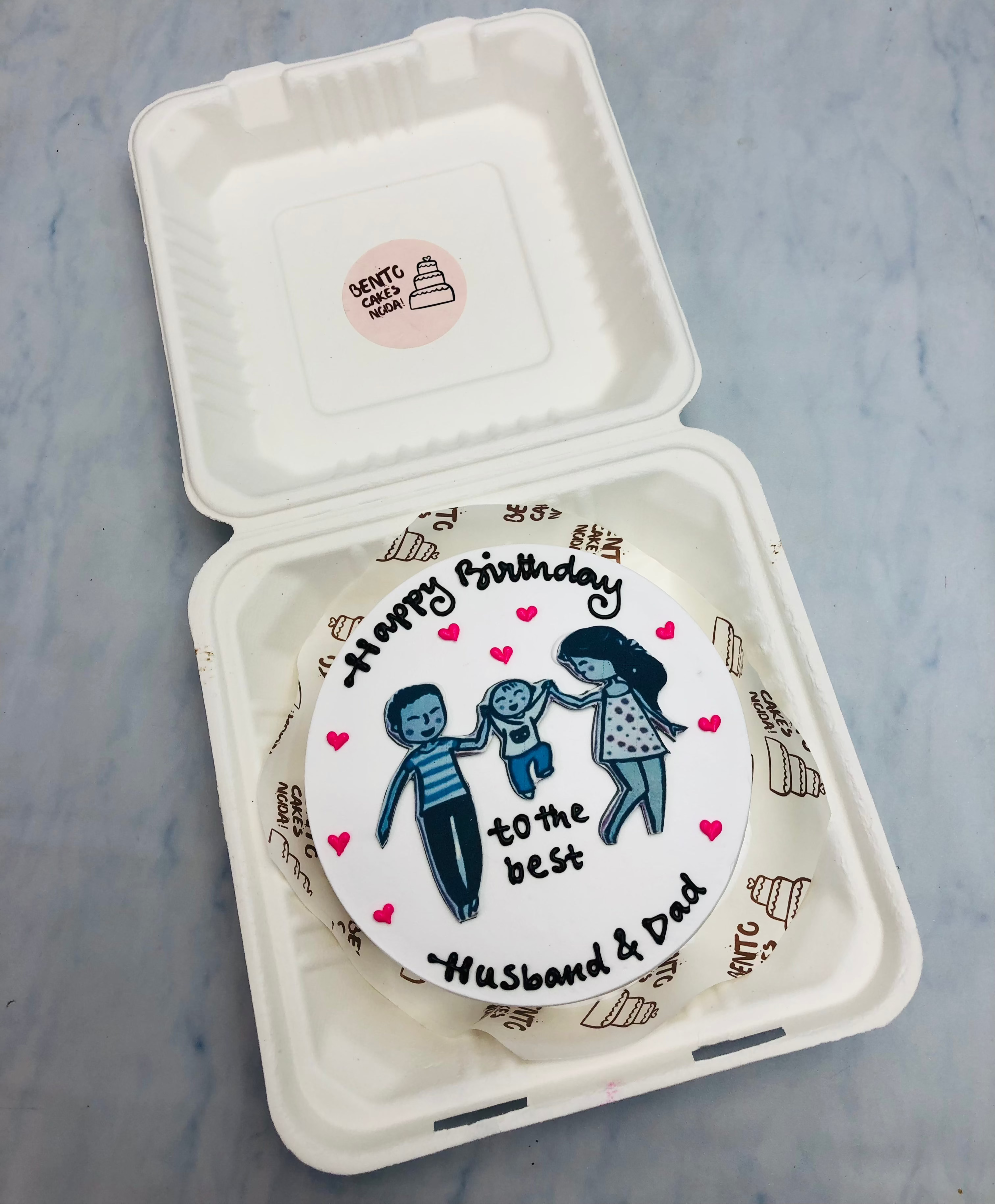 A white bento cake with a cute family sticker with father, mother and baby celebrating fathers birthday.