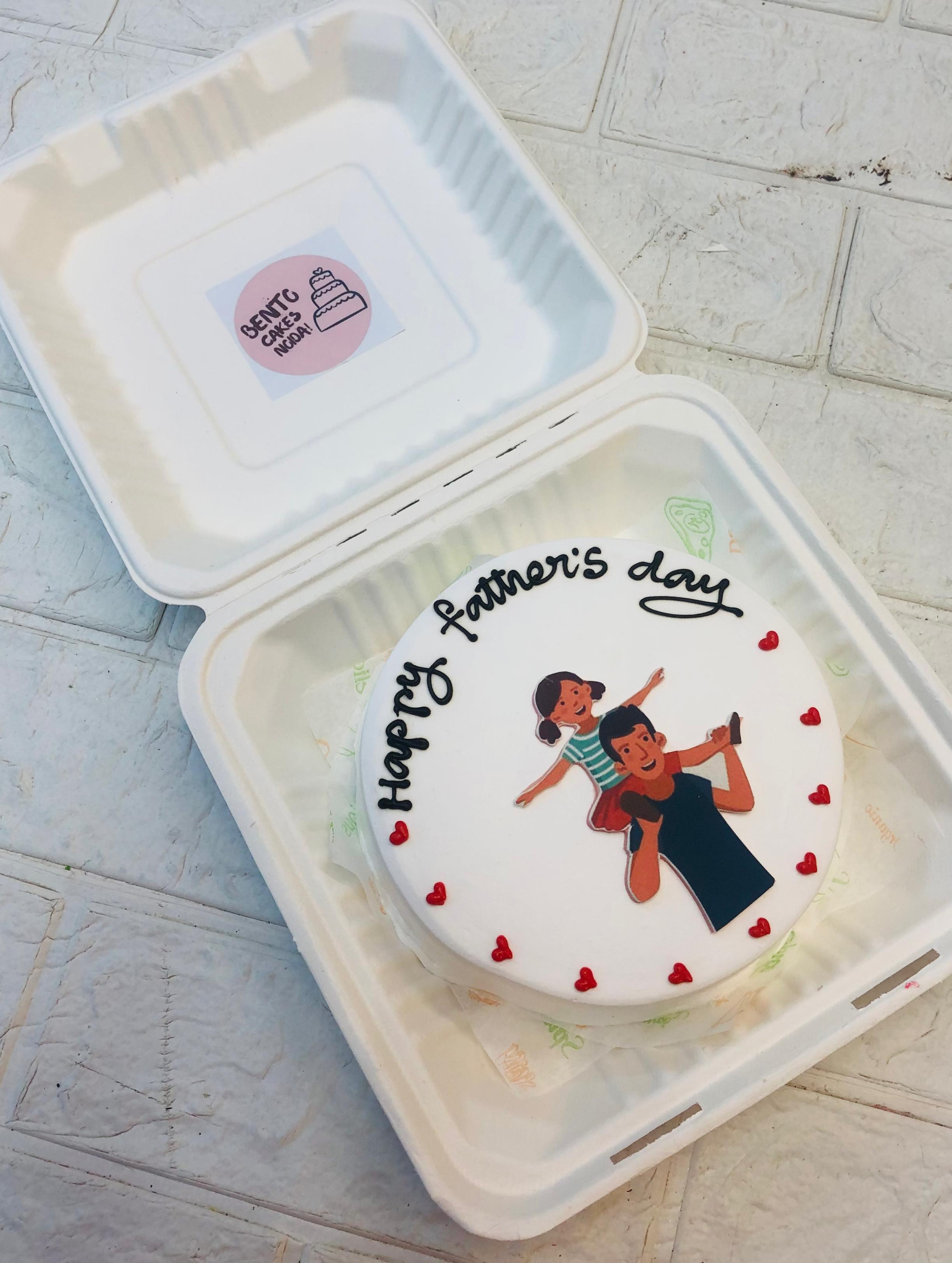 A beautifully decorated Father's Day cake inside a white box. The cake features an illustration of a father lifting his child, surrounded by red heart decorations. The message “Happy Father's Day” is written in black icing, creating a heartfelt touch.