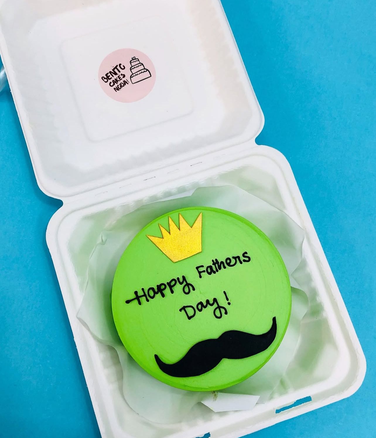 A green Father's Day cake decorated with a golden crown and black mustache, featuring "Happy Fathers Day!" written in black icing.