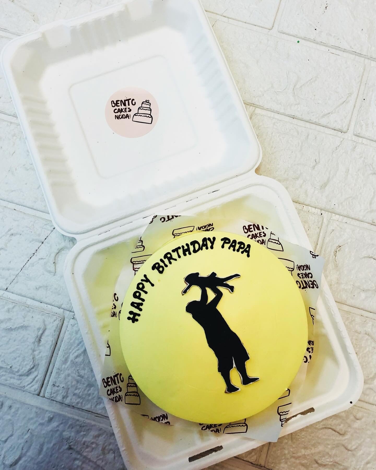 A light yellow bento cake is designed for fathers birthday with a baby and father print on it.