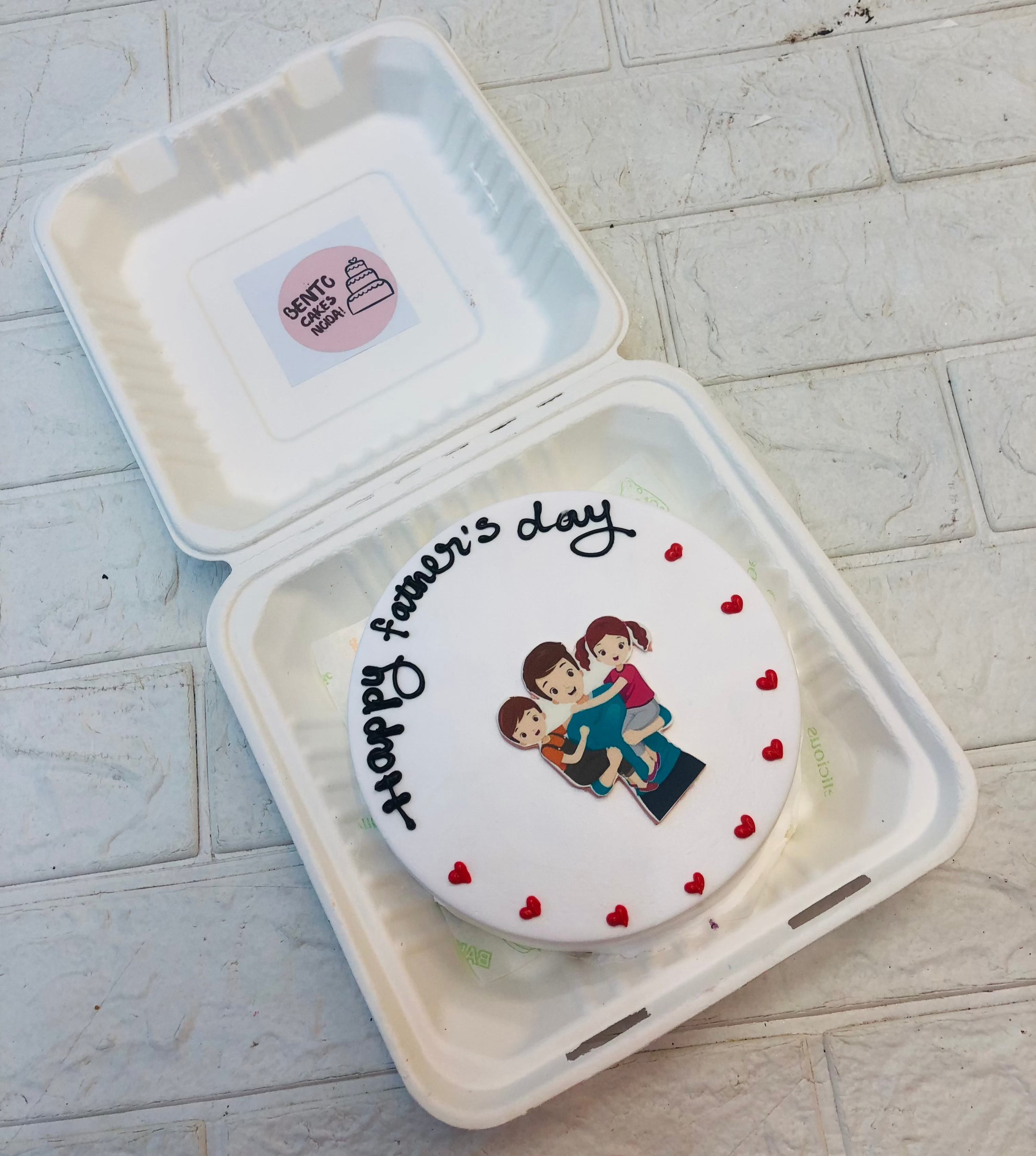 A white bento cake is designed for fathers day, a sticker iof 2 kids in father hands.