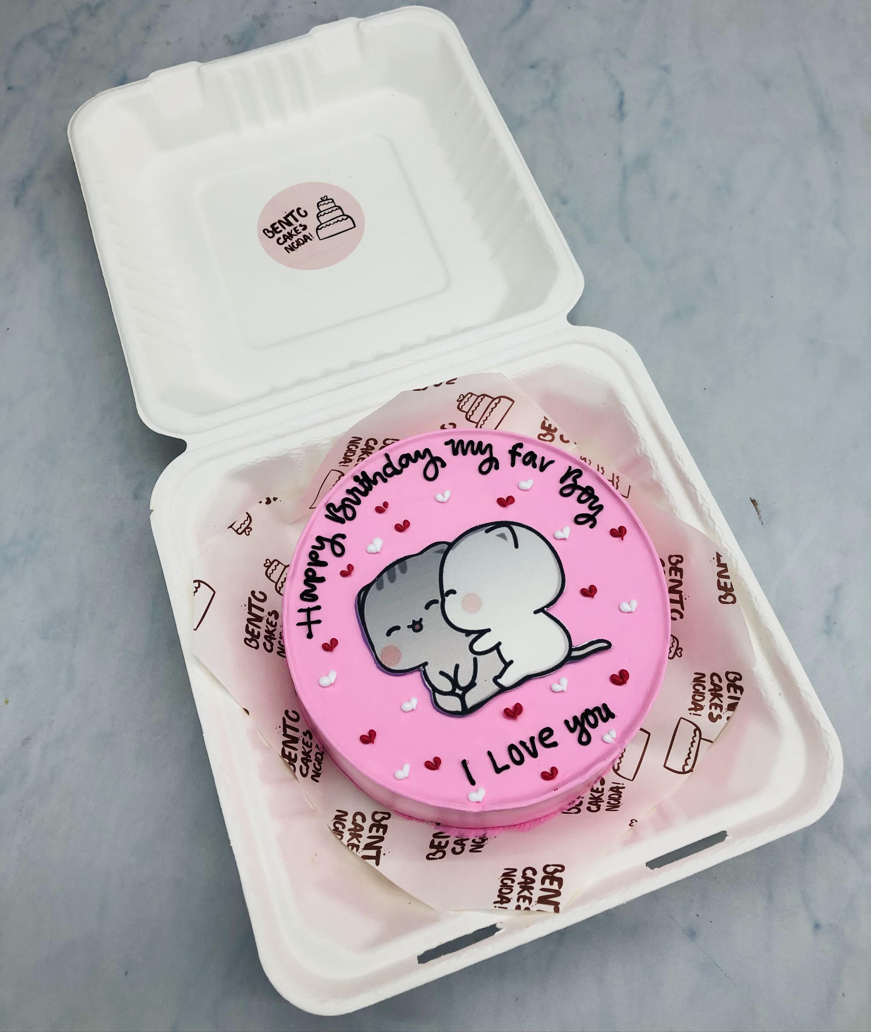 A pretty pink bento cake having kissing bubu dudu sticker and cake filled with little red, white hearts.