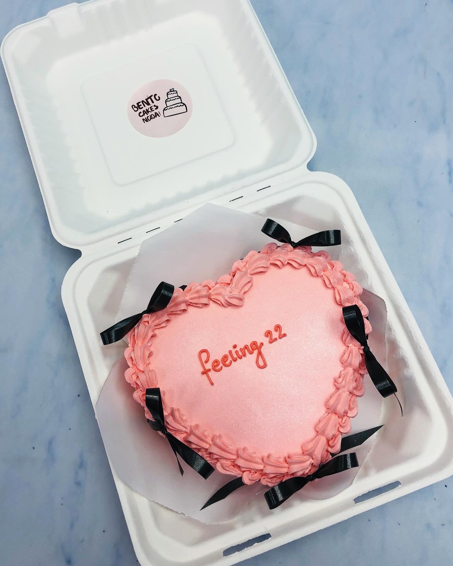 A peach color hearts shape bento cake decorated with black bows.