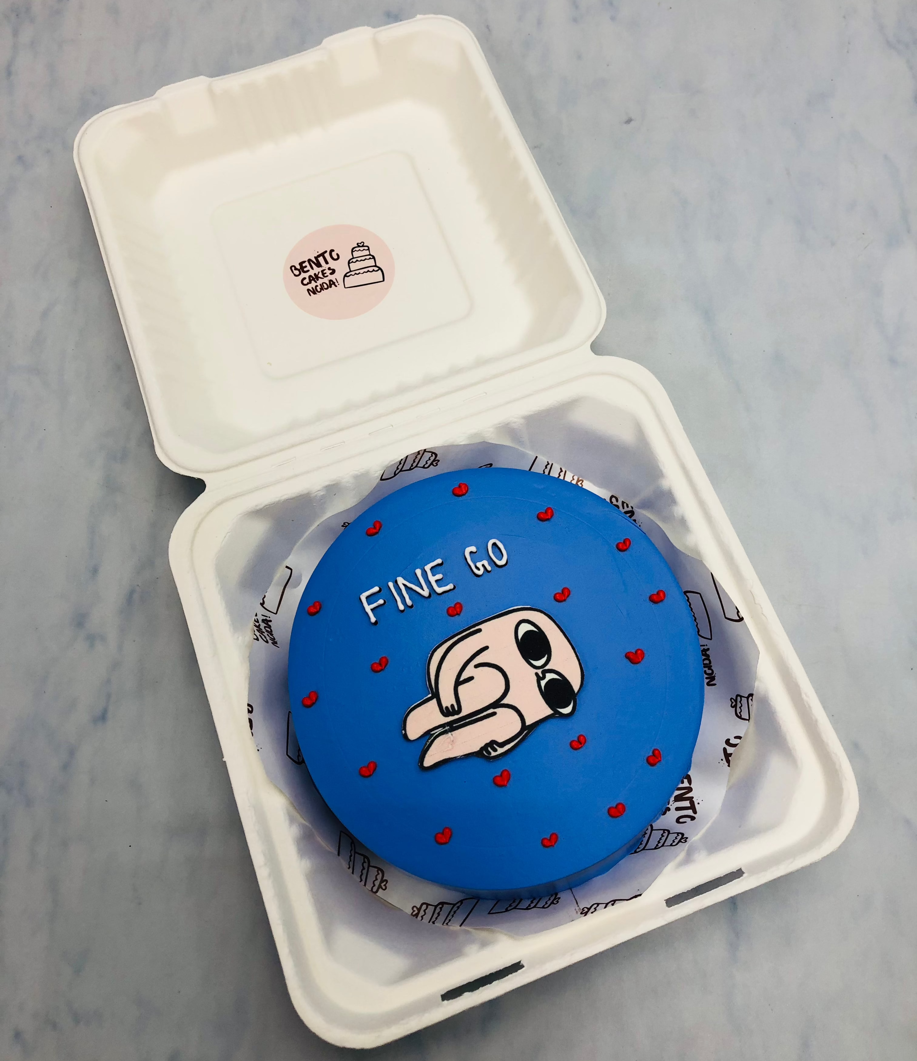 A dark blue bento cake decorated with little red hearts and a cartoon printed on it withy a "FINE GO" text.