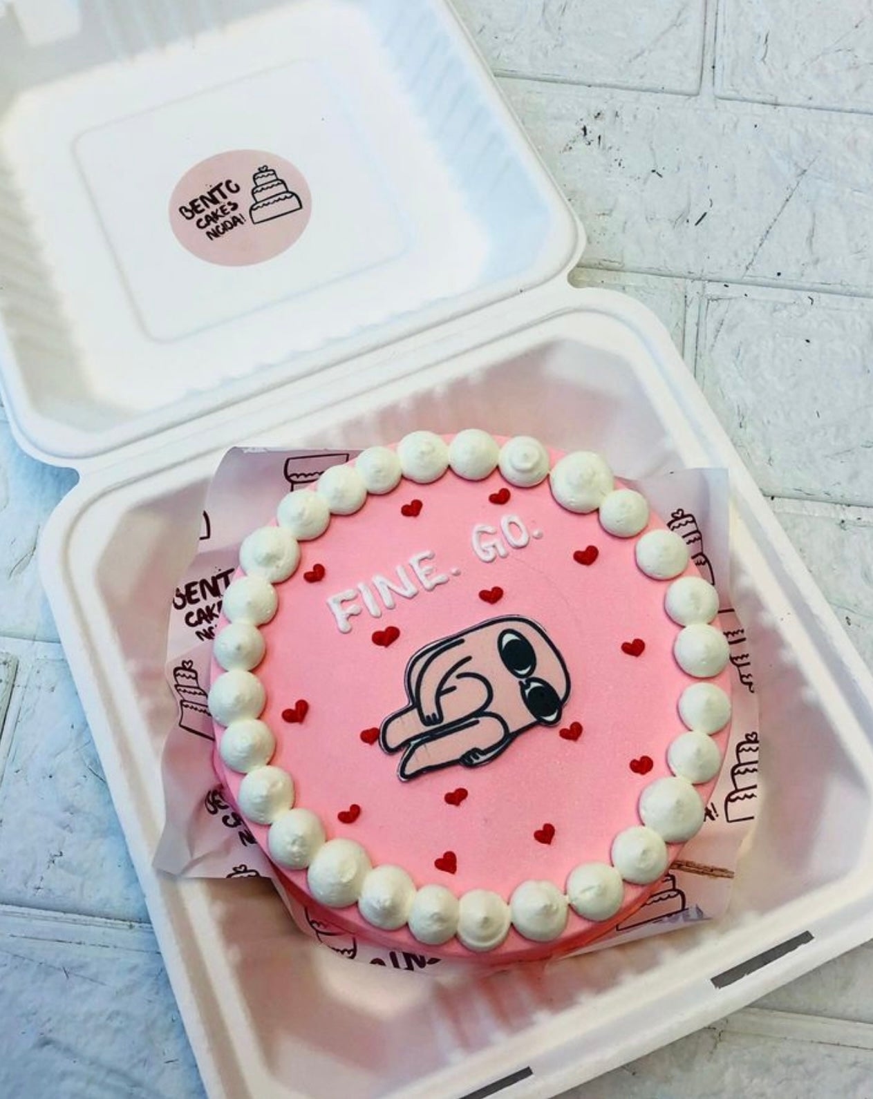 A light pink bento cake with litte red hearts and a cartoon character print with a "FINE GO" text with white color.