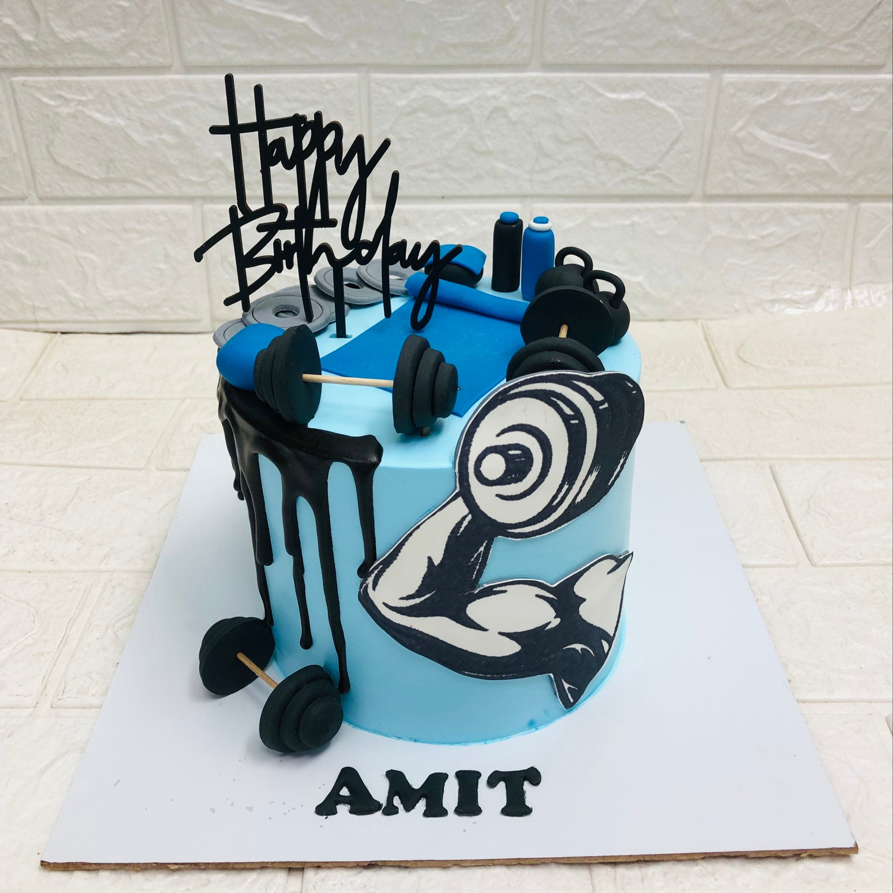 A blue and black birthday cake decorated with gym dumbbells and a barbell rod, perfect for a fitness enthusiast's special day.