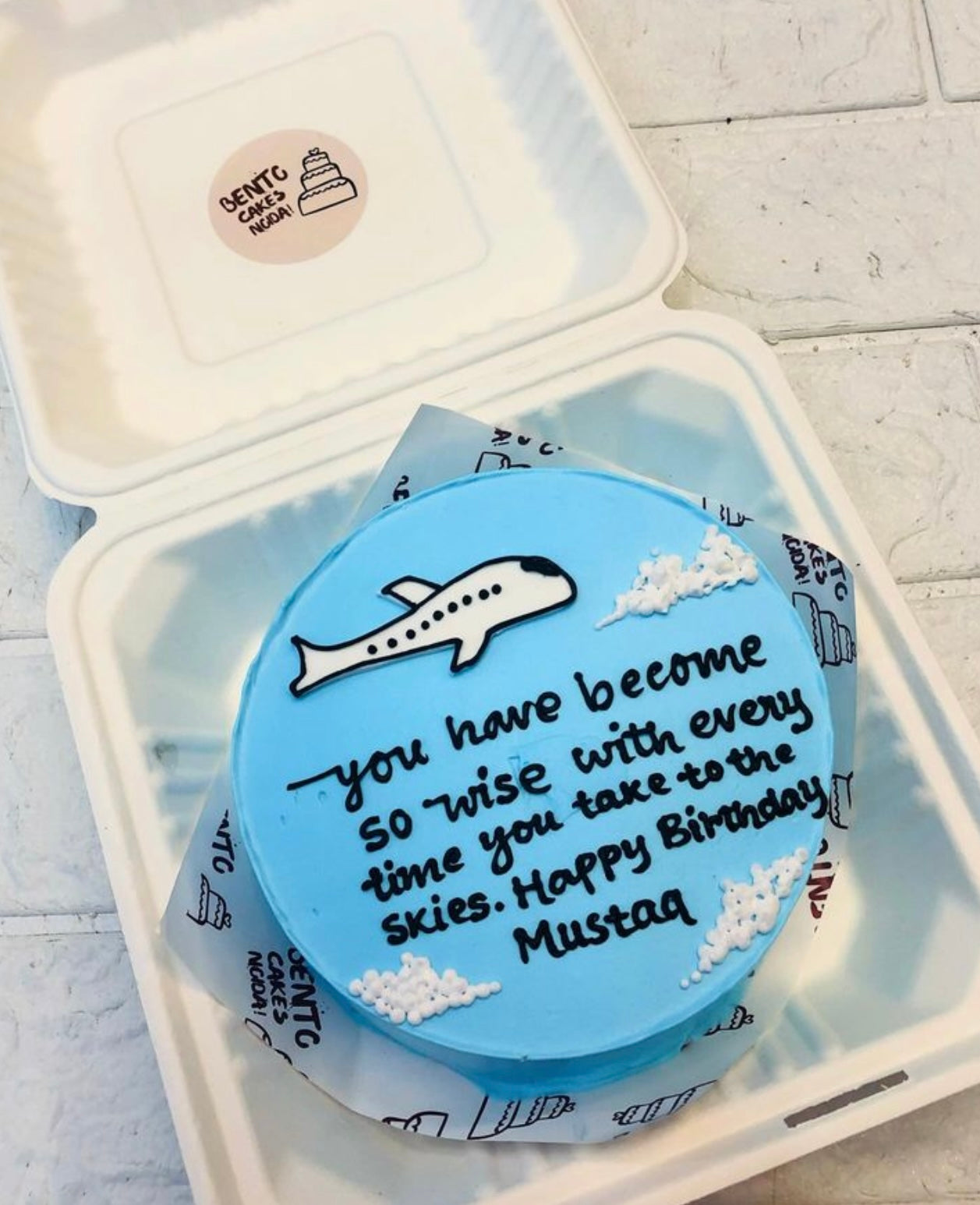 A skyblue bento cake with a flight traveller mens birthday cake, having a message written on it.