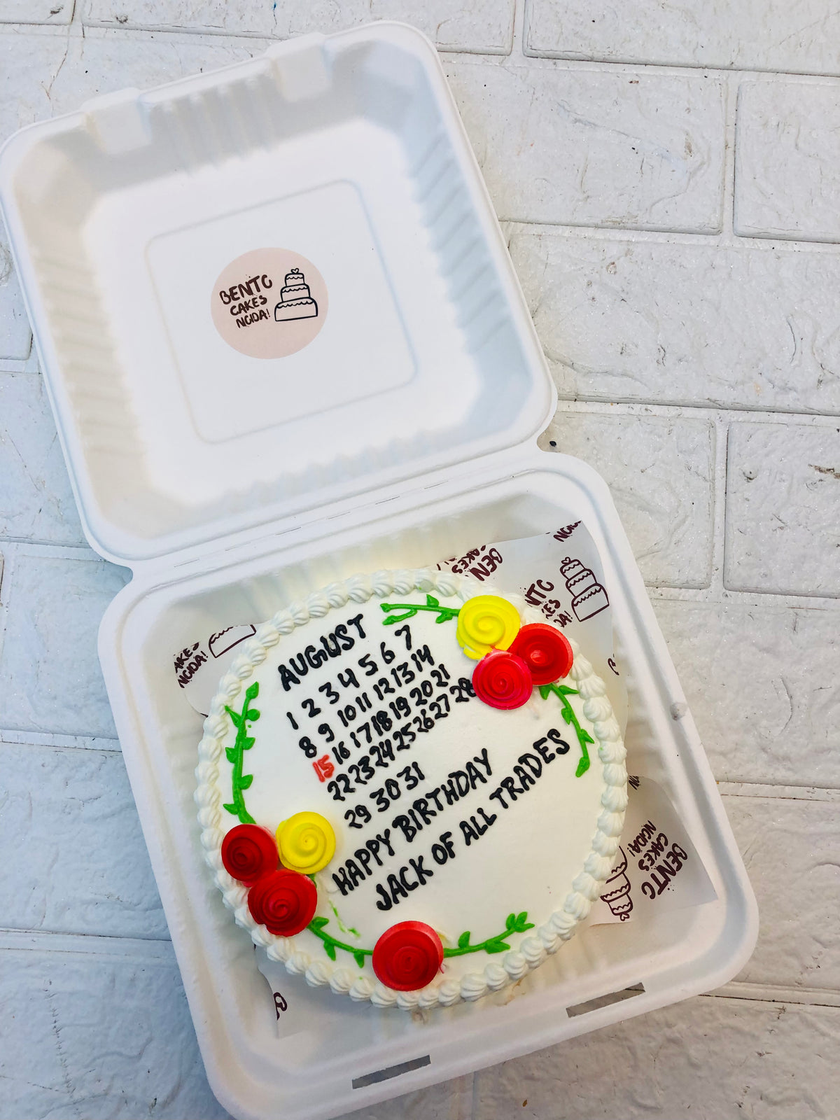 A white cake is decorated with a calendar design of may month on it and some colorful floral designed on it.