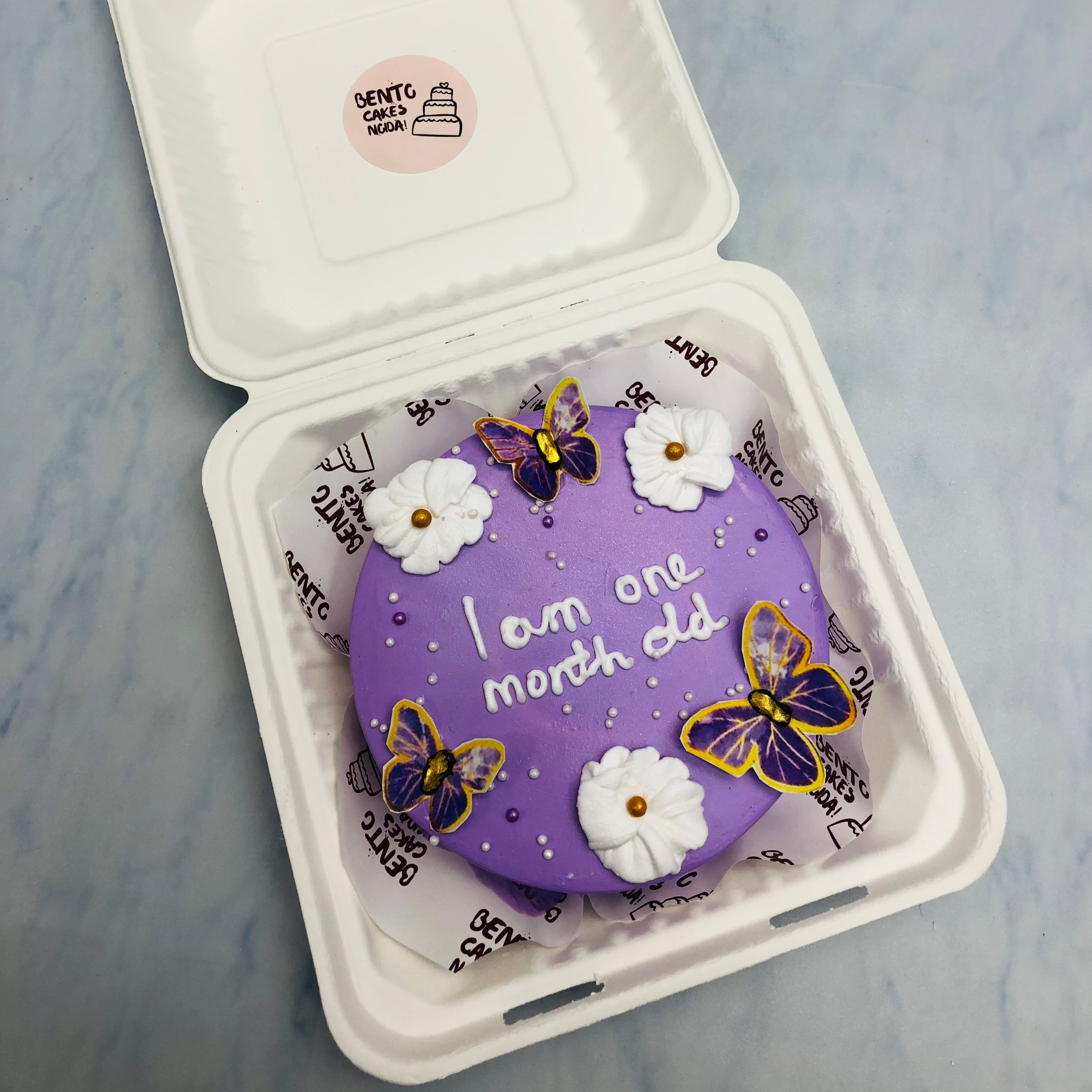A dark purple bento cake with blue butterflies and white floral design on it.