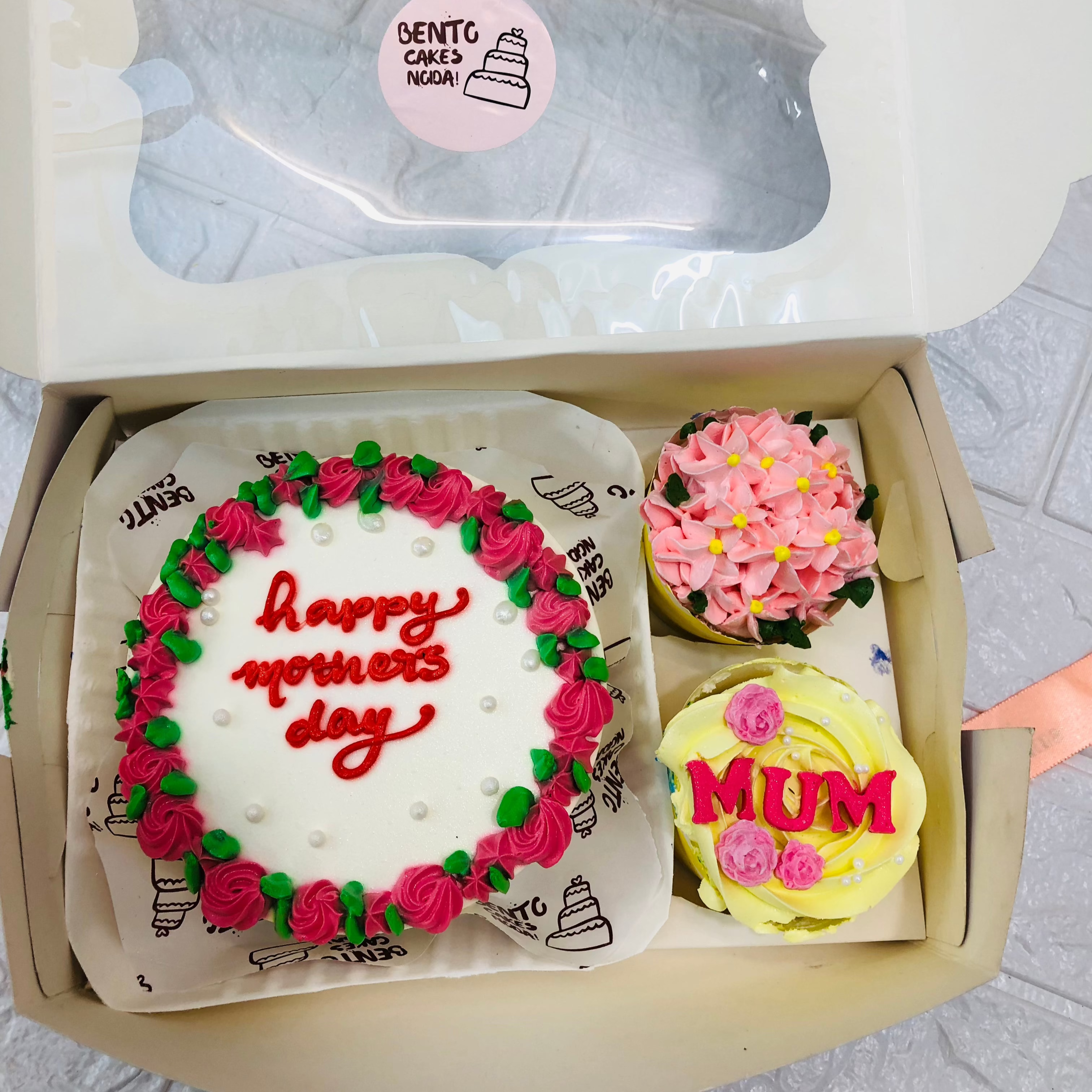 A box containing 1 cake and 2 cupcakes set. A cake with pink floral design and "Happy Mother's Day" text written on it, cupcakes having pink and yellow floral design.