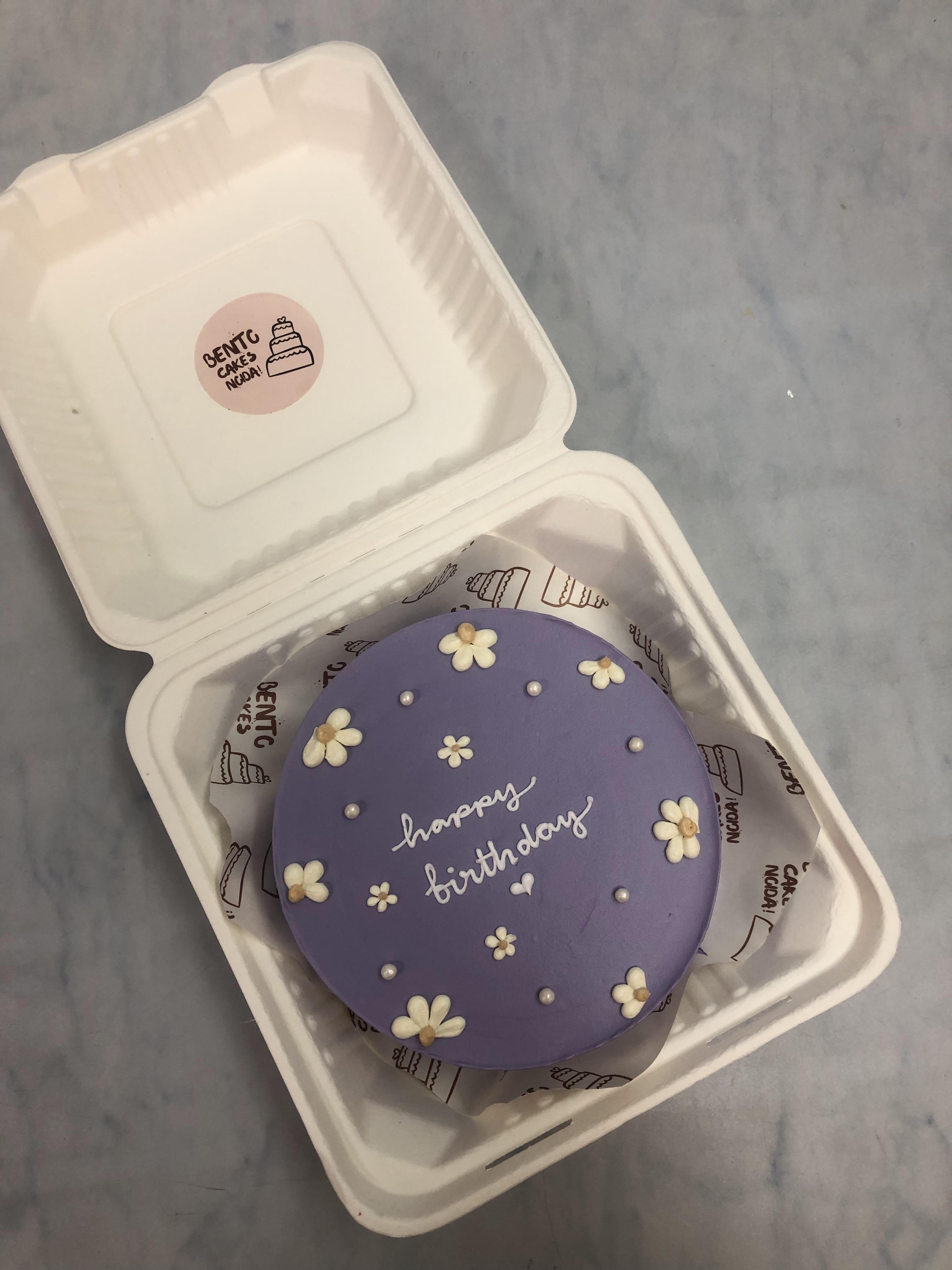 A purple frosting bento cake decorated with preety white floral and white sprinkles for birthday.