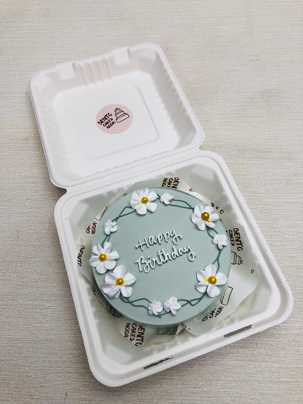 A grey cake with aesthetic floral design and happy birthday text on it.