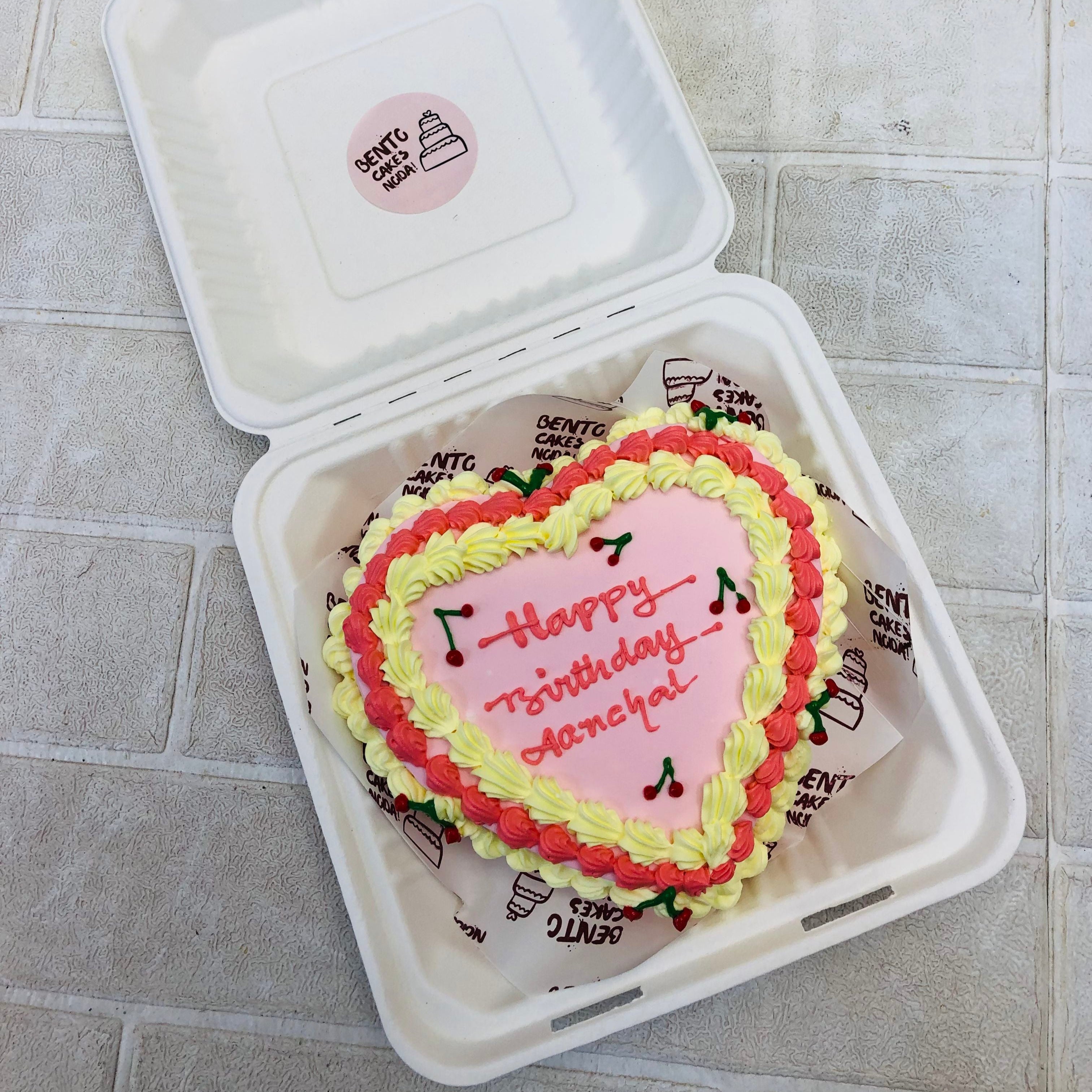 A lighrt pink heart shape cake decorated with red and yellow truffle design.