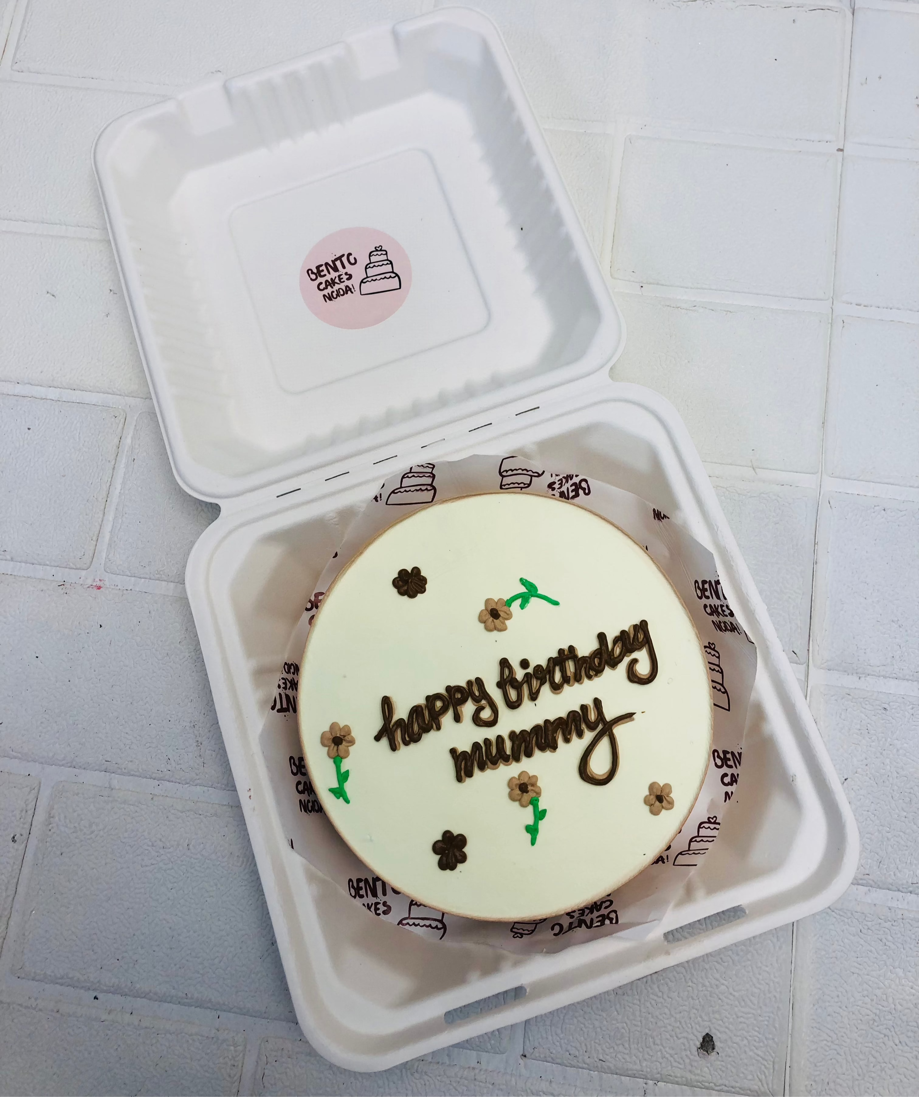 A white bento cake with brown and coffee color florals design on it with a "happy birthday mummy" text with brown icing.