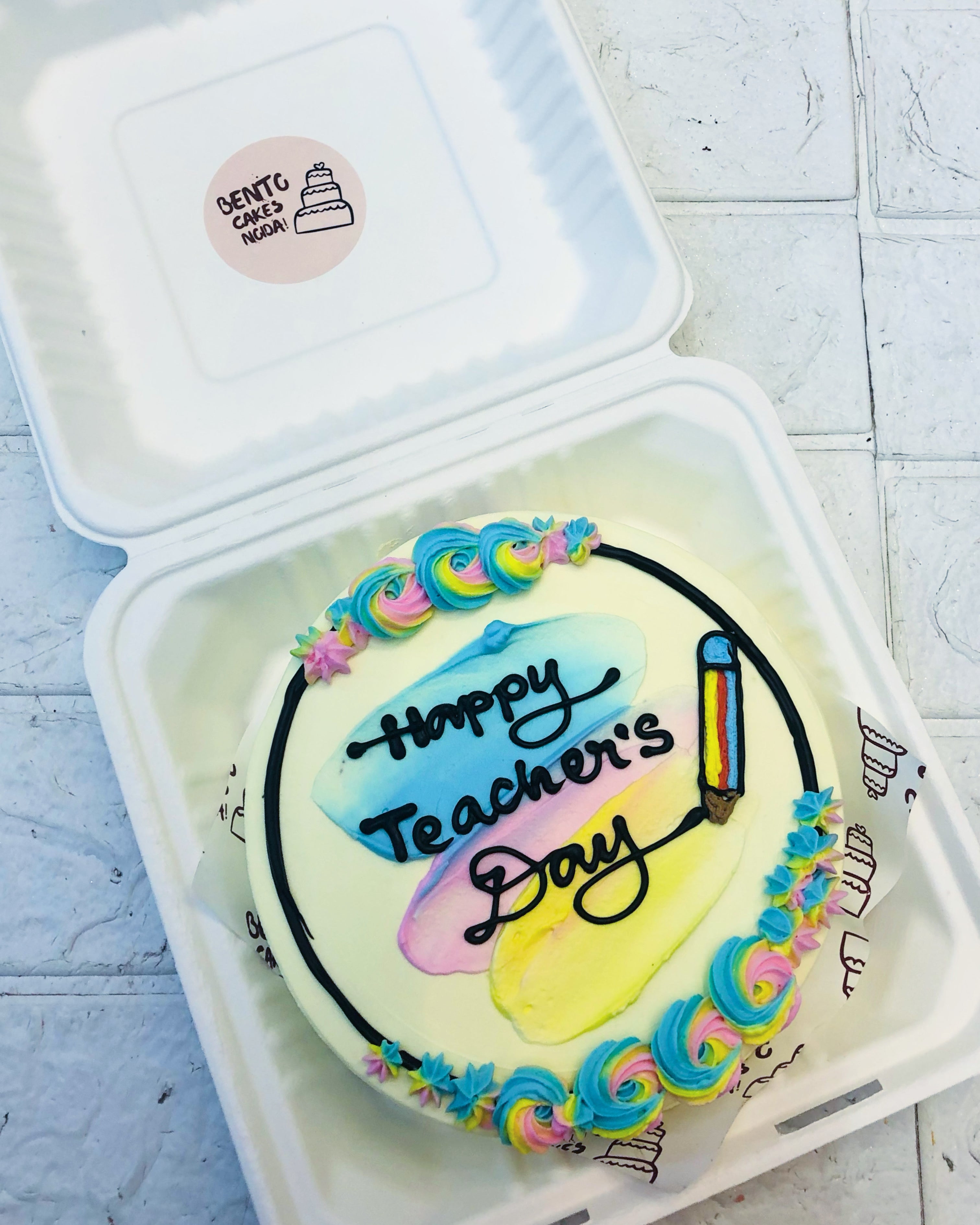A white bento cake with rainbow color floral design with a text of "Happy Teachers Day".