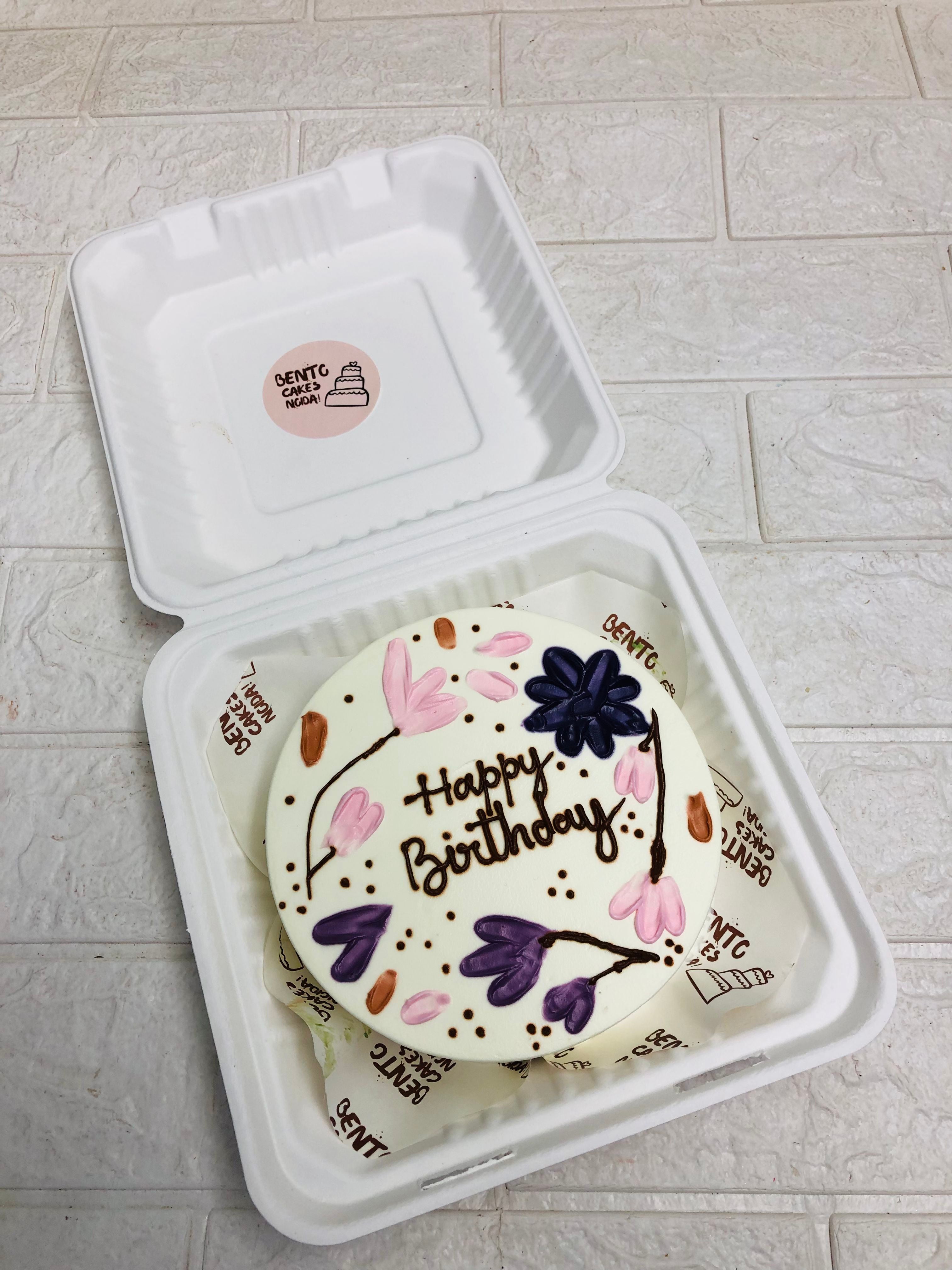 A birthday cake placed inside a bento box, showcasing its colorful frosting and decorative elements.