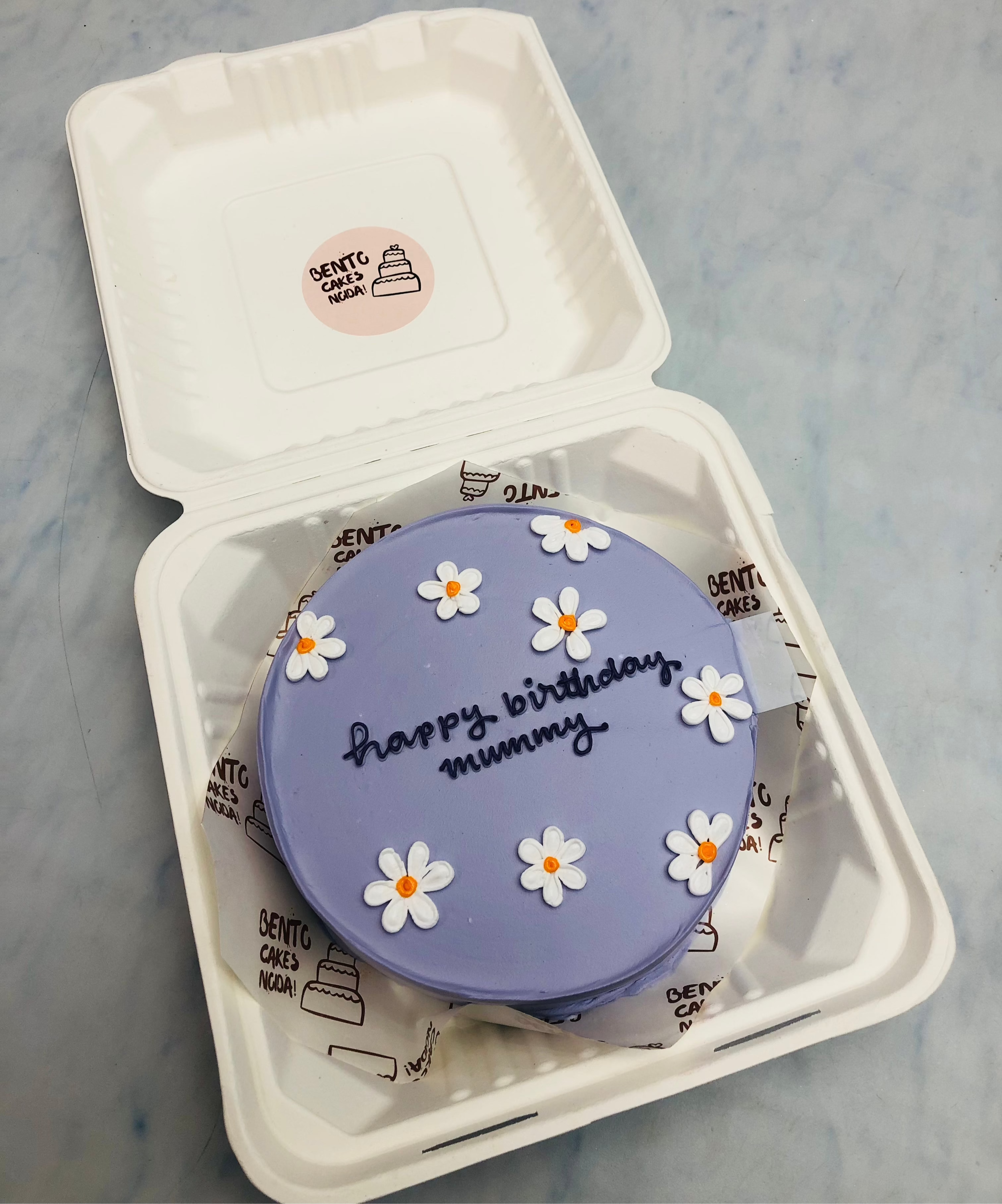 A purple bentyo cake having white florals design for mothers birthday.