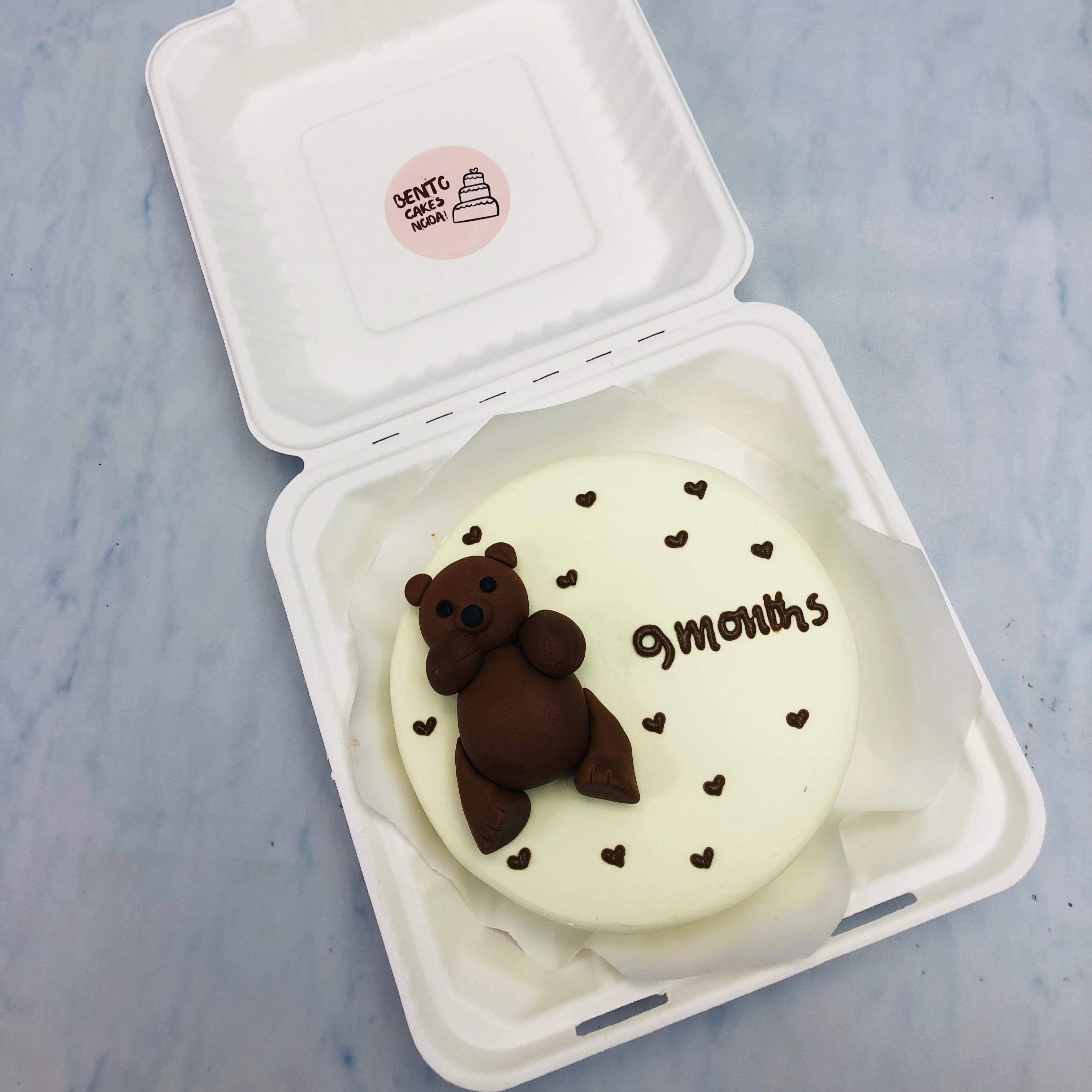 An offwhite cake with brown fondant teddy bear and filled with brown little hearts.